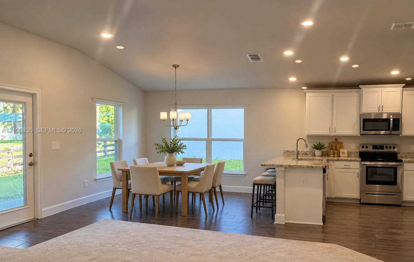 187 NW 45th Loop, Ocala, FL 34475 Open-concept kitchen and dining area featuring vaulted ceilings, recessed lighting, wood-finish flooring, white shaker-style cabinetry, and stone-surface countertops