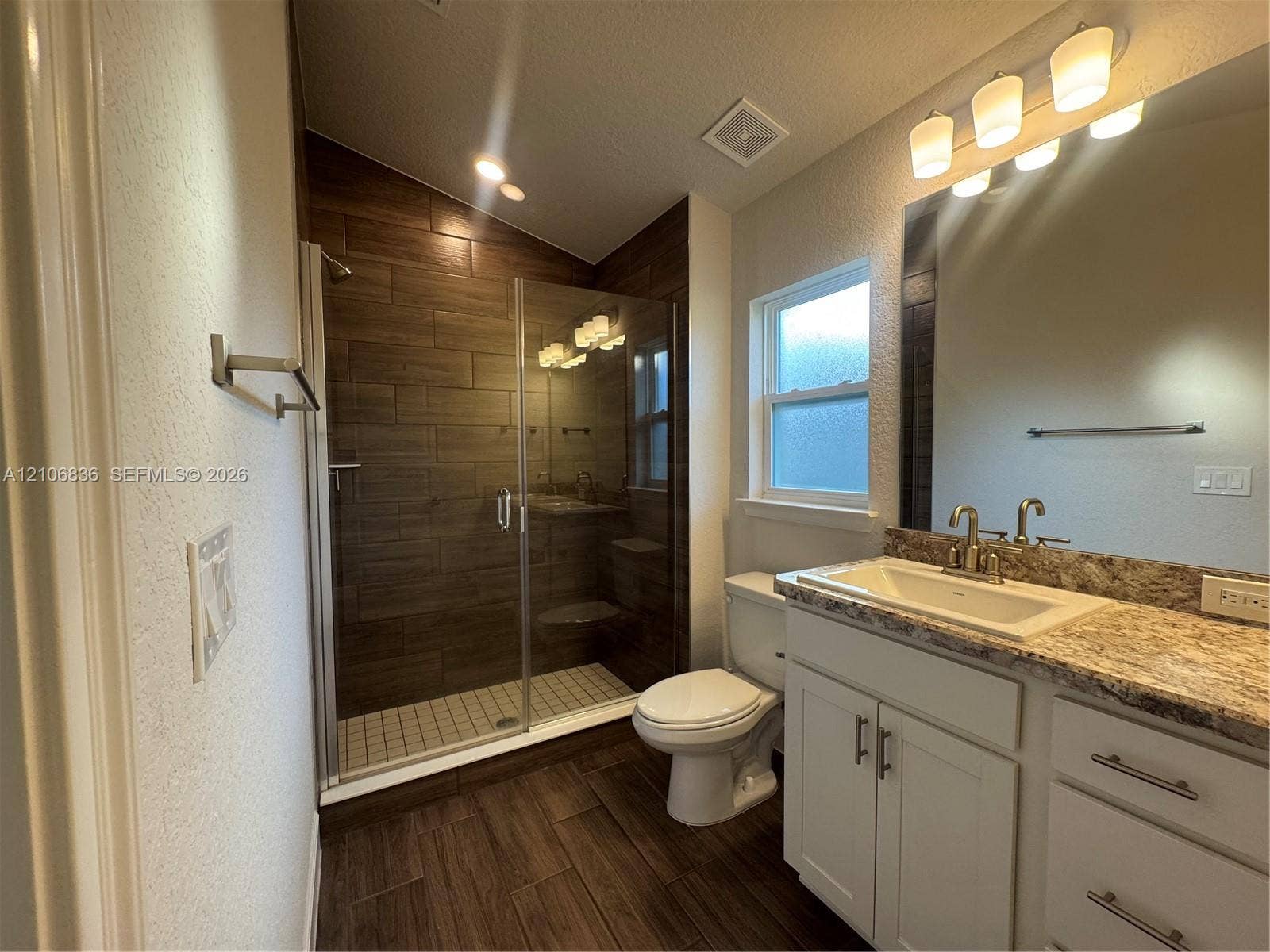 187 NW 45th Loop, Ocala, FL 34475 Bathroom featuring a walk-in shower with glass enclosure, wood-finish tile wall surround, stone-composite countertop, white vanity cabinetry with brushed-metal hardware, and wood-finish flooring