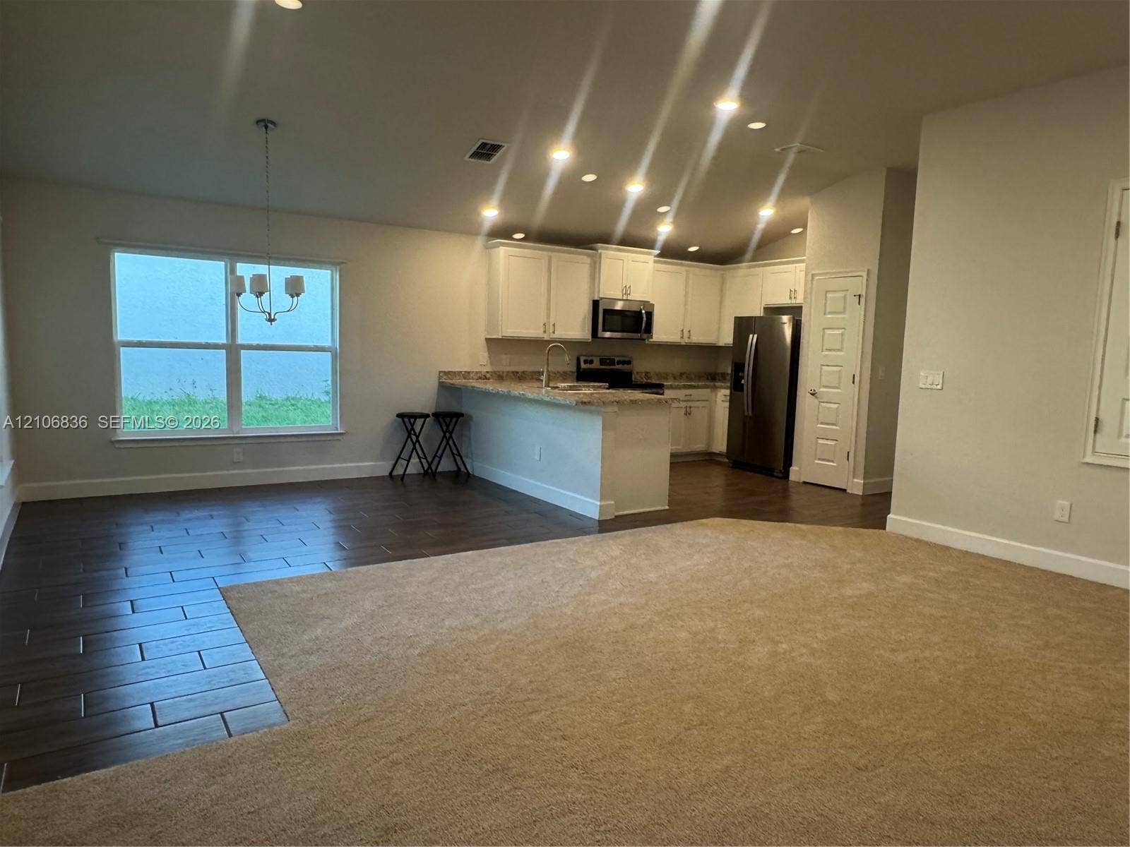 187 NW 45th Loop, Ocala, FL 34475 Open-concept living space featuring wood-finish tile flooring, neutral carpeting, white shaker-style cabinetry, a breakfast bar with stone-finish countertops, and stainless steel appliances