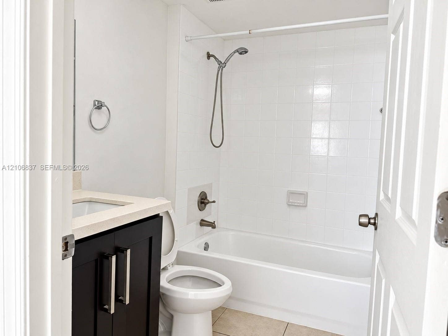 Bathroom featuring a dark wood-finish vanity with a light-toned countertop, a shower and tub combination with tiled surround, and a wall-mounted handheld shower fixture