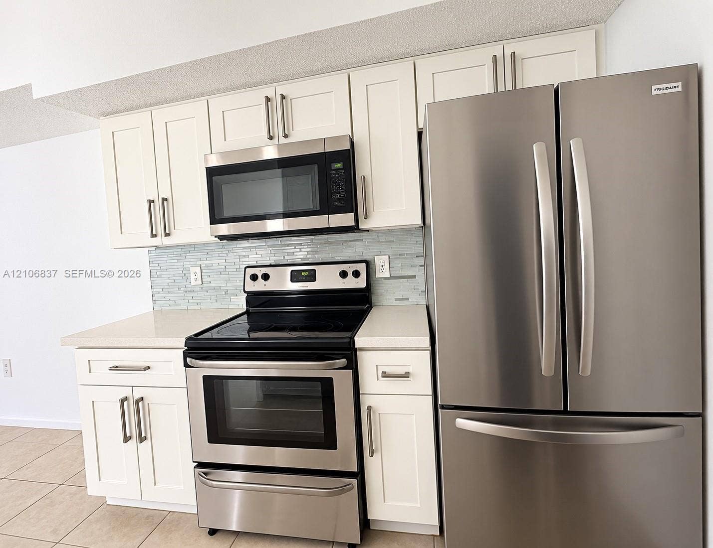 Kitchen featuring white shaker-style cabinetry, stainless steel appliance suite, quartz countertops, and a glass-tile backsplash