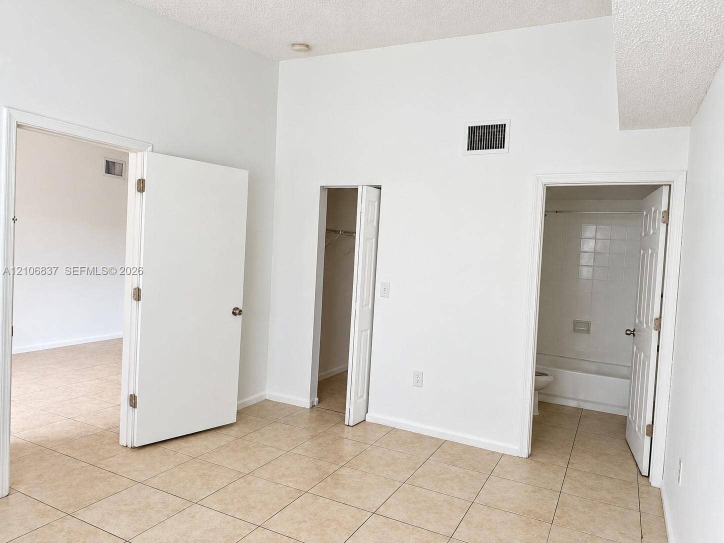 Room featuring tile flooring, vaulted ceilings, and a built-in closet, with access to a bathroom containing a tiled shower-tub enclosure