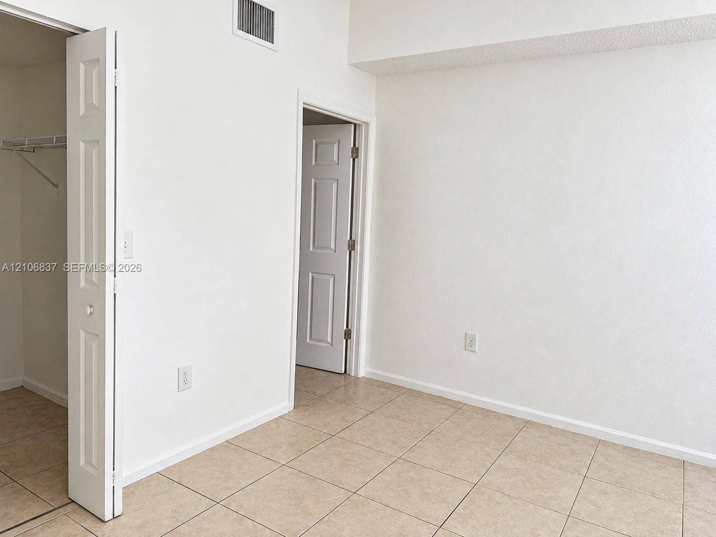 Interior space featuring neutral wall-to-wall tile flooring, white panel doors, and a built-in closet with wire shelving
