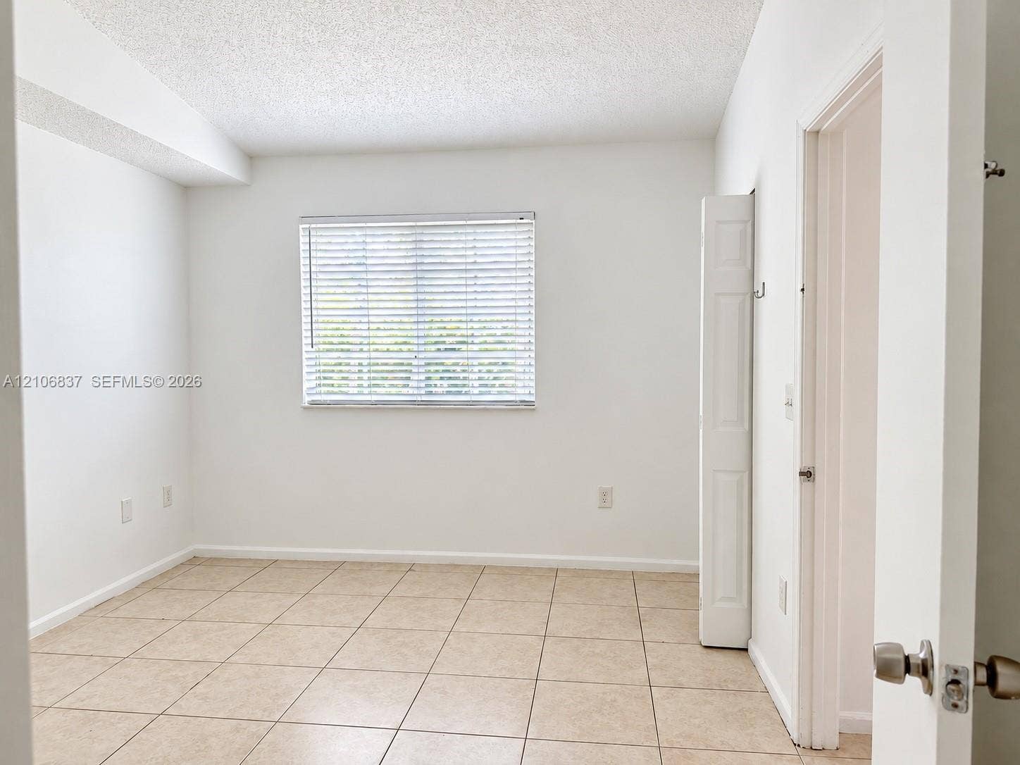Neutral-toned ceramic tile flooring, horizontal window blinds, and bi-fold closet doors