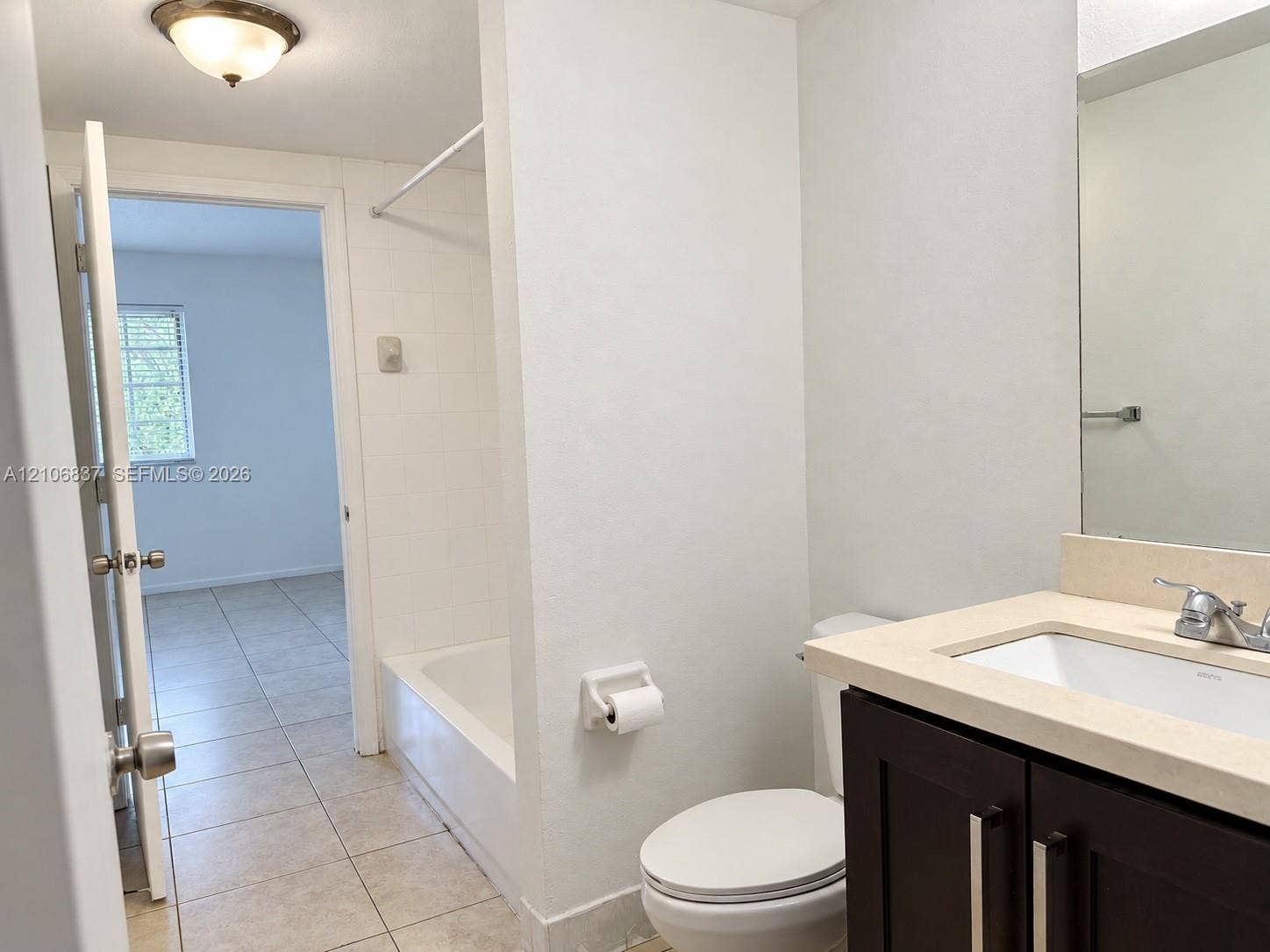 Bathroom featuring a vanity with a light-toned countertop, a tub-shower combination with tiled surround, and ceramic tile flooring
