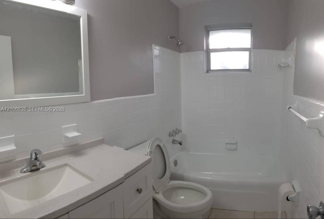 Bathroom featuring a white vanity cabinet, solid-surface countertop with an integrated basin, white subway tile tub surround, and a framed wall mirror