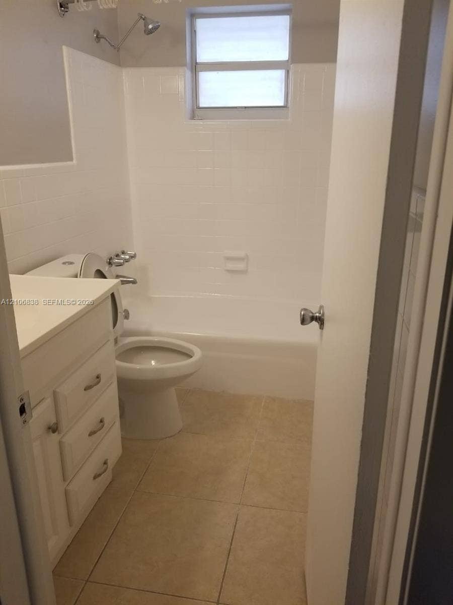 Bathroom featuring a white vanity with integrated basin, tiled shower-tub combination, ceramic floor tile, and a wall-mounted shower fixture