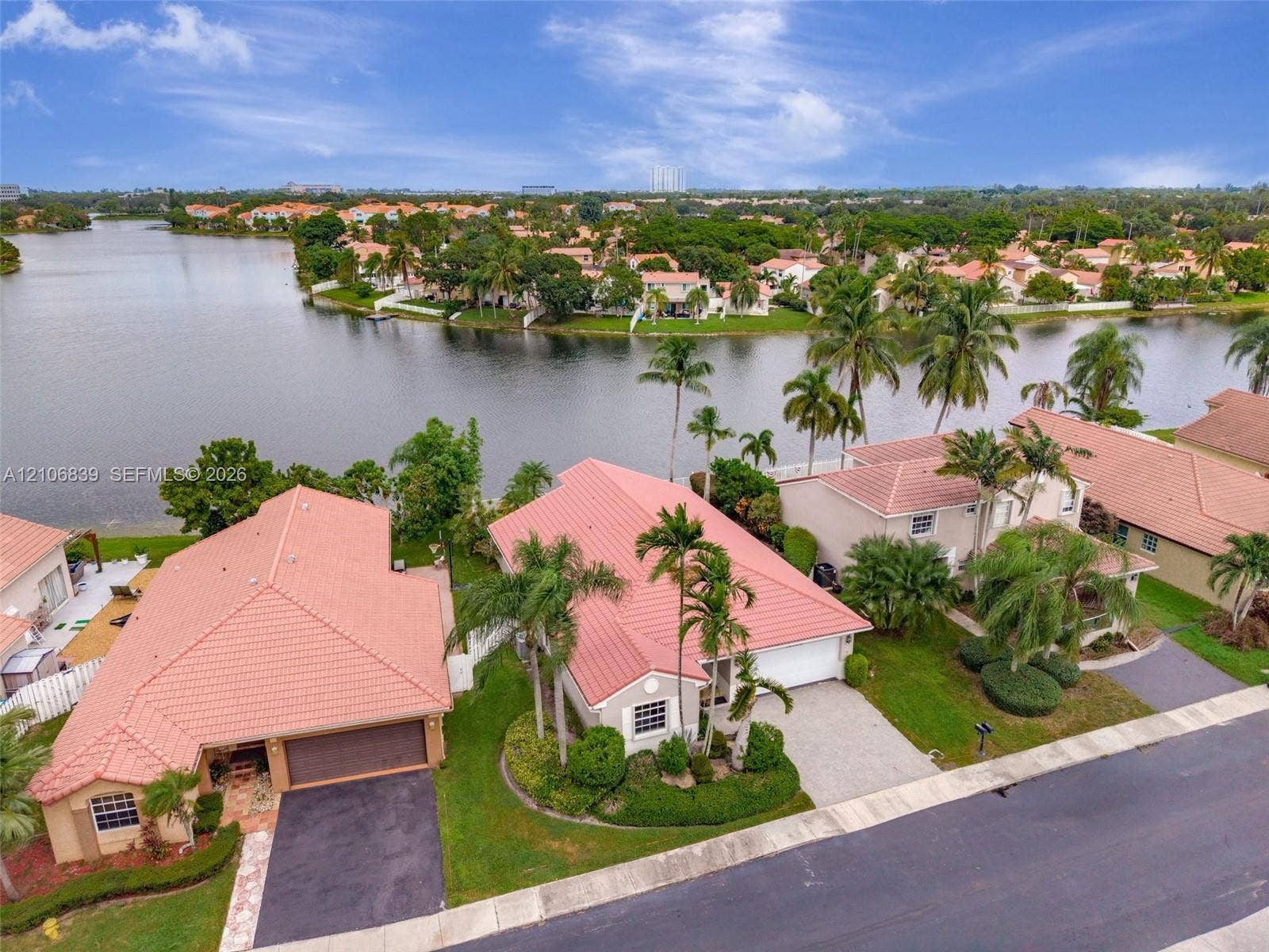 12683 NW 11th Place, Sunrise, FL 33323 Waterfront property featuring tile roofing, paved driveways, mature palm landscaping, and attached multi-car garages