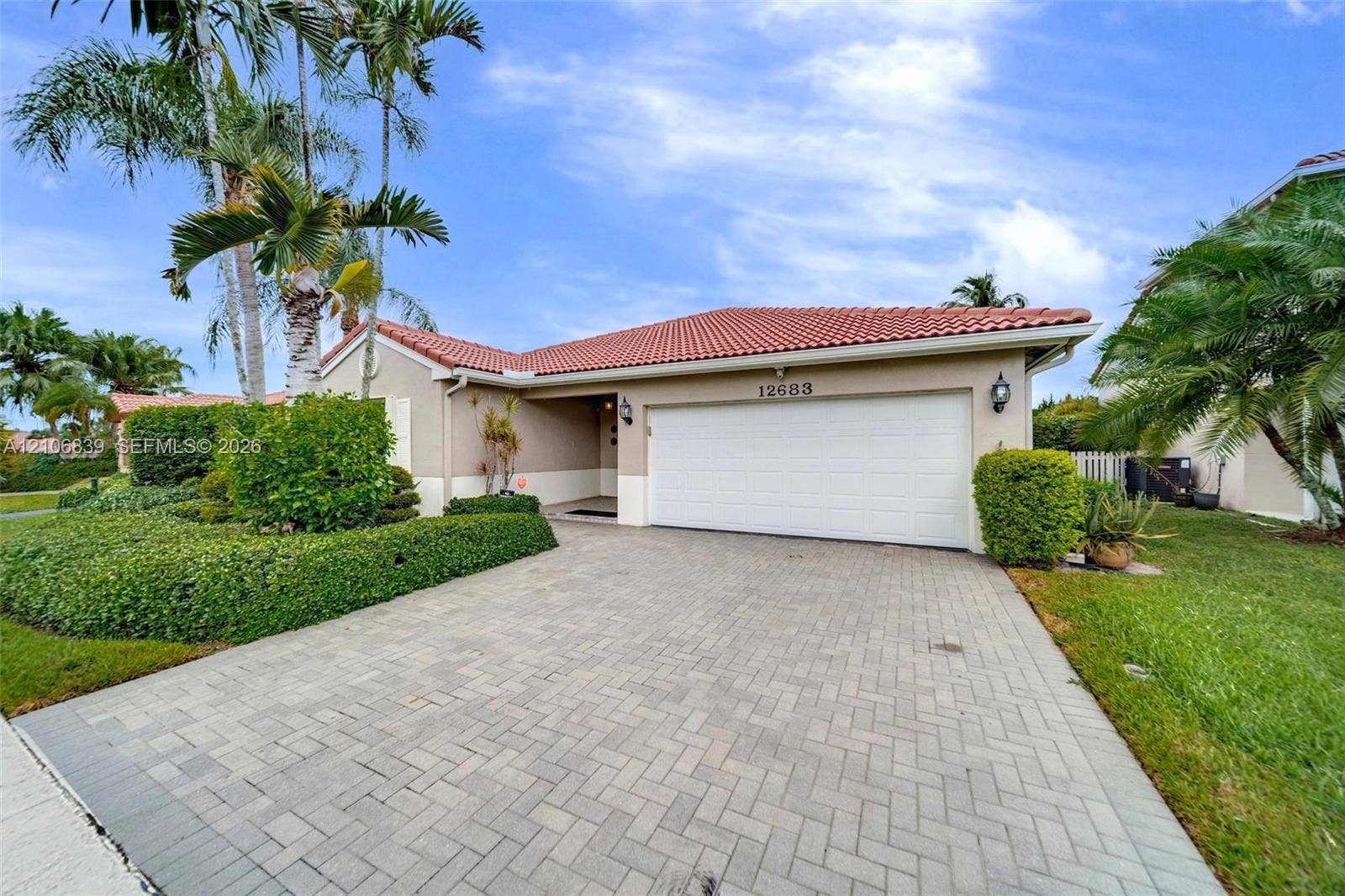 12683 NW 11th Place, Sunrise, FL 33323 Exterior featuring a tile roof, paver driveway, two-car garage, and established landscaping with palm trees