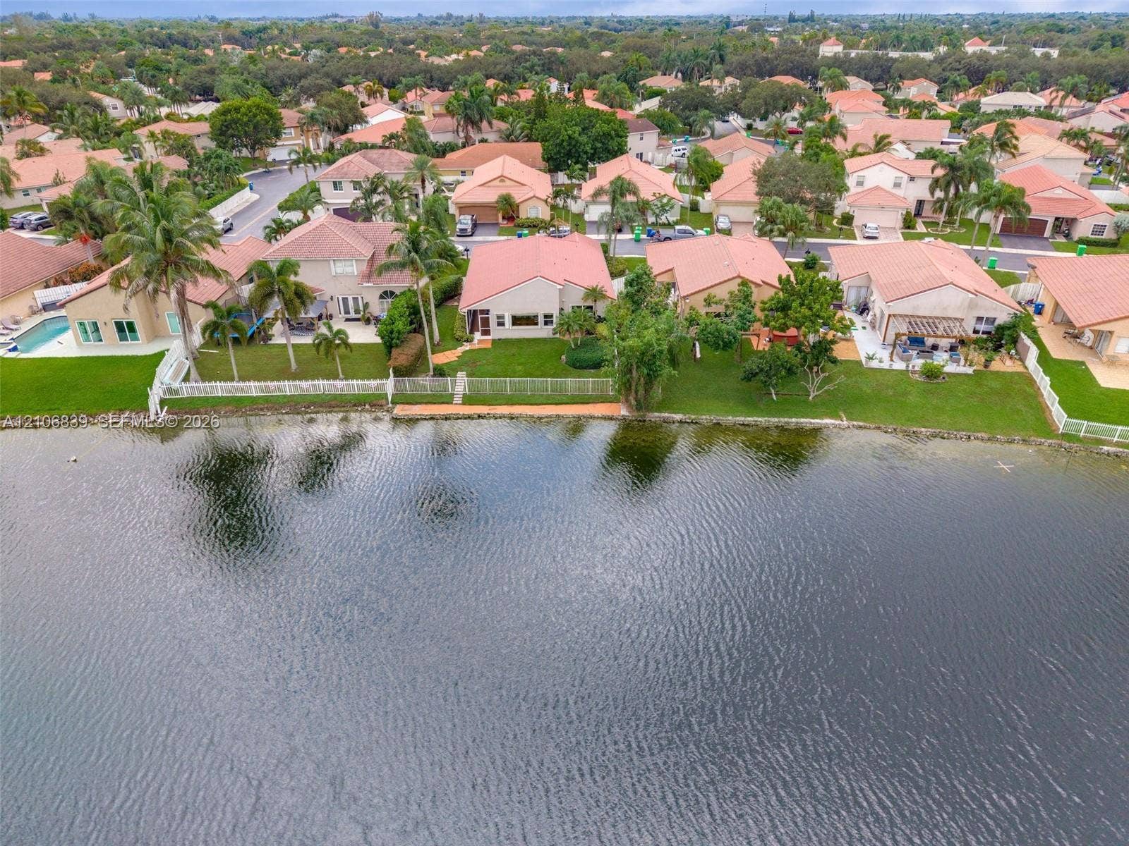 12683 NW 11th Place, Sunrise, FL 33323 Waterfront residential property featuring a manicured lawn, white perimeter fencing, and mature palm trees