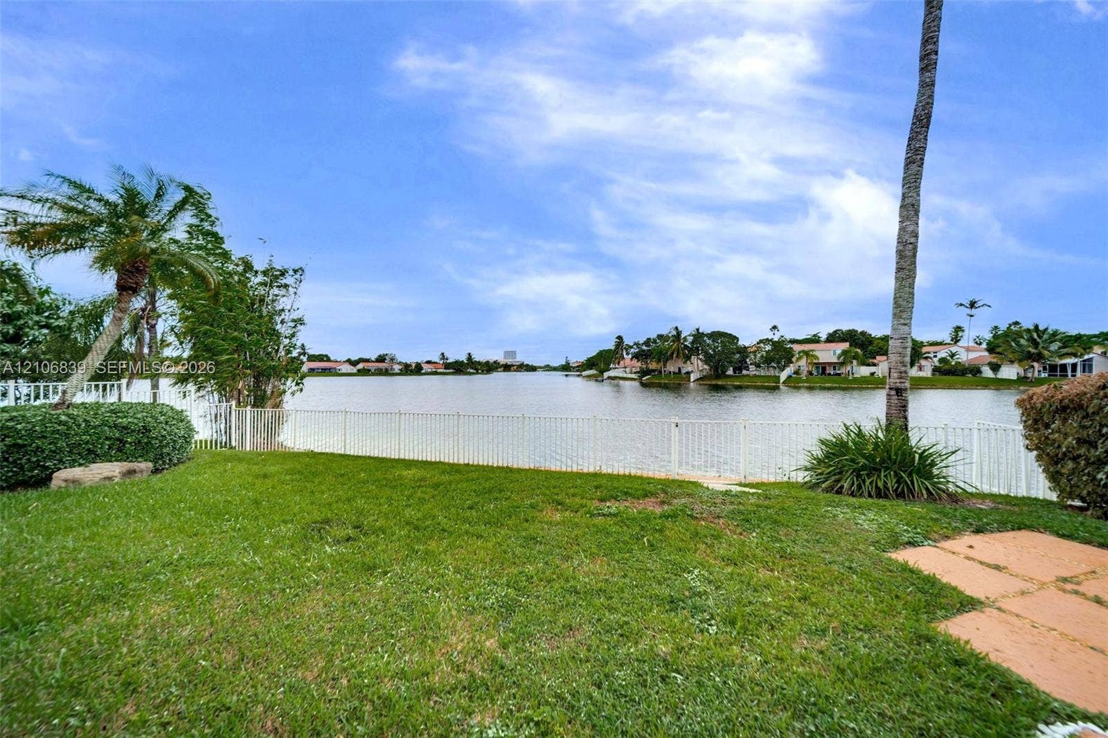 12683 NW 11th Place, Sunrise, FL 33323 Waterfront backyard featuring a manicured lawn, perimeter fencing, and mature palm trees
