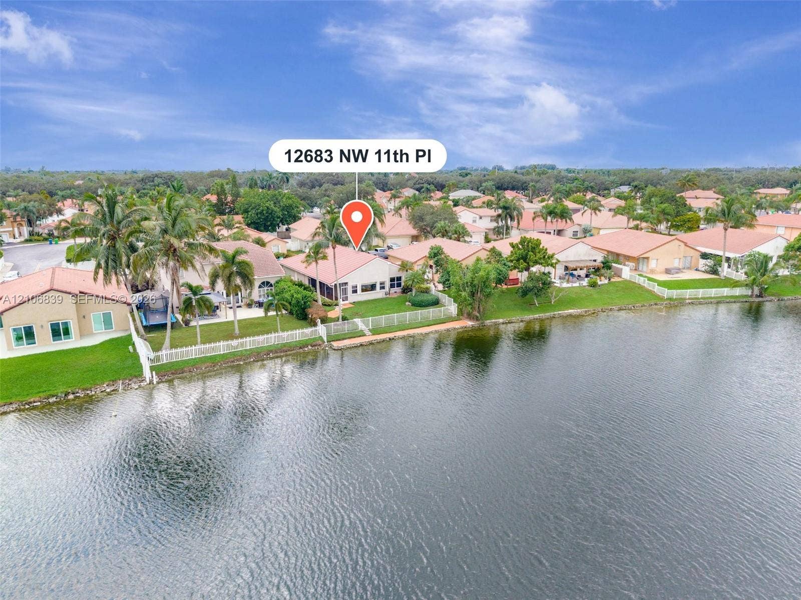 12683 NW 11th Place, Sunrise, FL 33323 Waterfront residence featuring a tiled roof, screened-in patio, and manicured lawn with mature palm trees