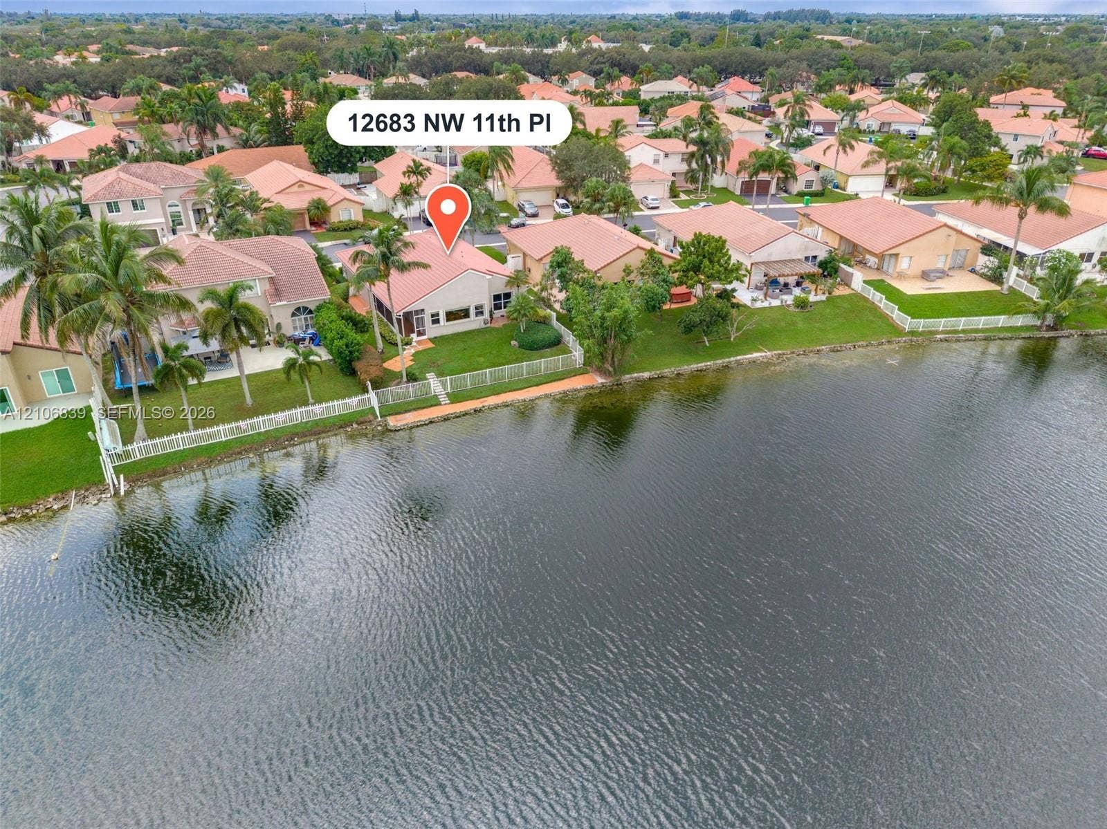 12683 NW 11th Place, Sunrise, FL 33323 Waterfront property featuring a private lawn, perimeter fencing, and mature palm trees