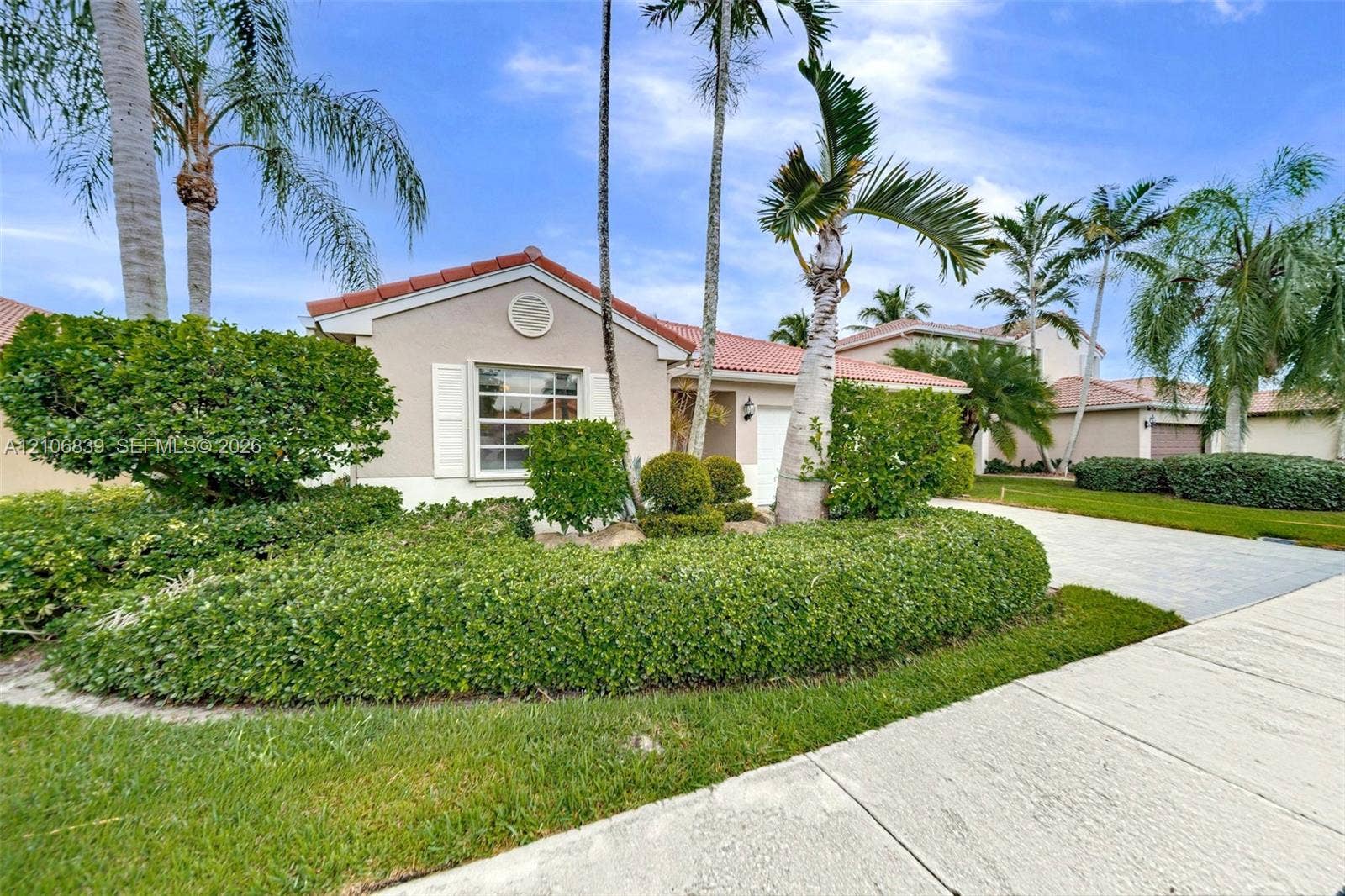 12683 NW 11th Place, Sunrise, FL 33323 Exterior facade featuring a tile roof, stucco siding, and a paved driveway, complemented by mature landscaping and palm trees