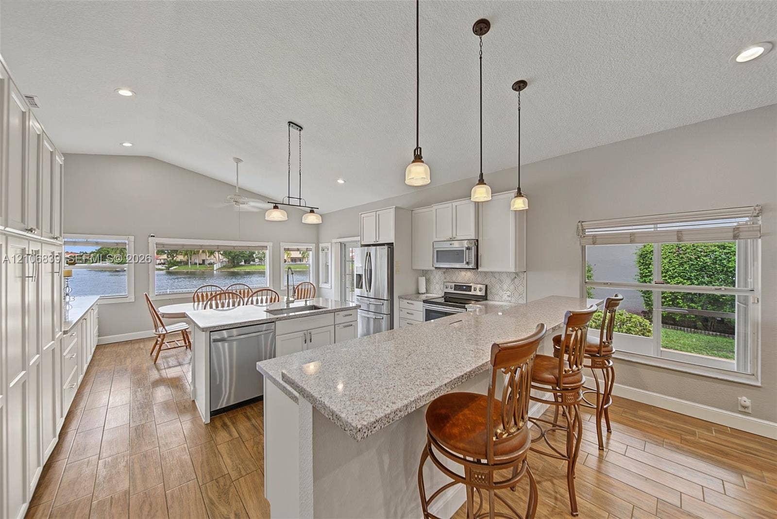 12683 NW 11th Place, Sunrise, FL 33323 Kitchen featuring wood-finish flooring, quartz-surround island with breakfast bar, stainless steel appliances, white cabinetry, and pendant lighting