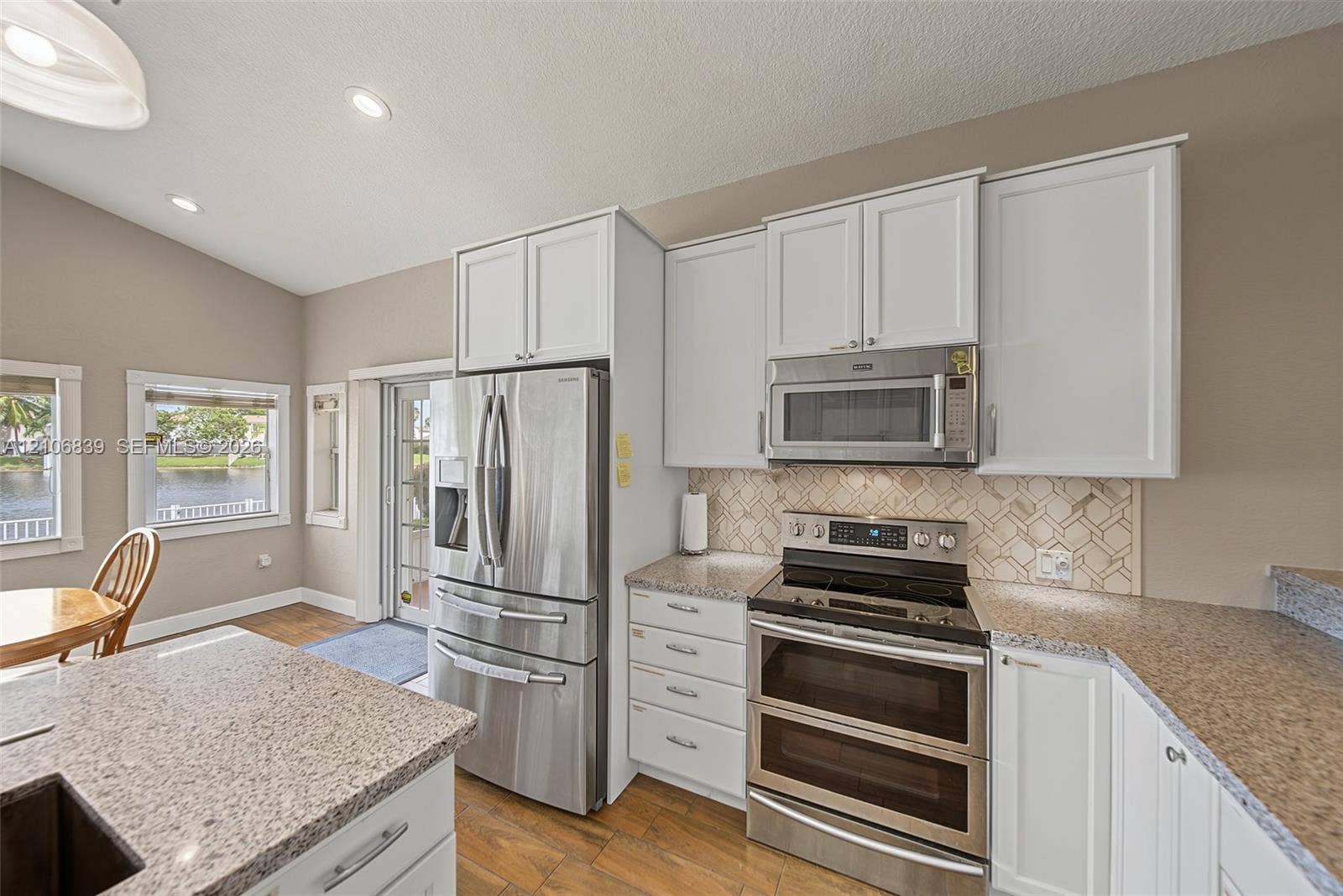 12683 NW 11th Place, Sunrise, FL 33323 Kitchen featuring white cabinetry, stainless steel appliances, speckled stone-finish countertops, geometric-patterned backsplash, and wood-finish tile flooring