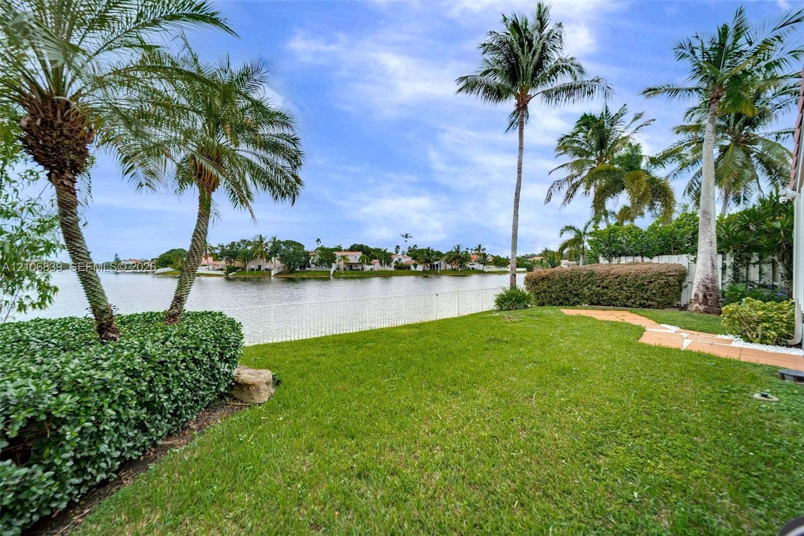 12683 NW 11th Place, Sunrise, FL 33323 Waterfront backyard featuring a manicured lawn, palm trees, mature hedges, and a white perimeter fence