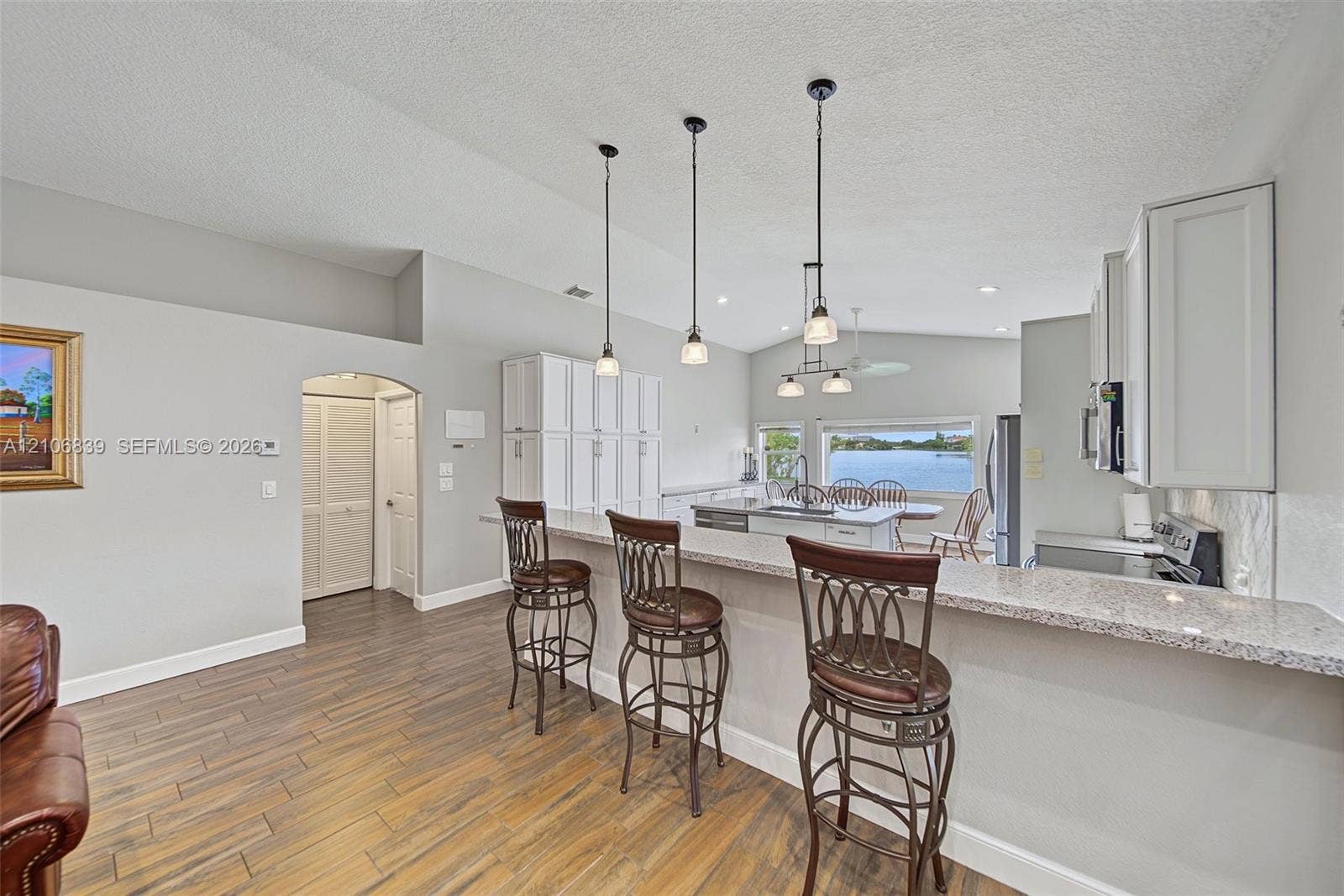 12683 NW 11th Place, Sunrise, FL 33323 Kitchen featuring a tiered countertop, wood-finish flooring, white cabinetry, decorative pendant lighting, and water scenery