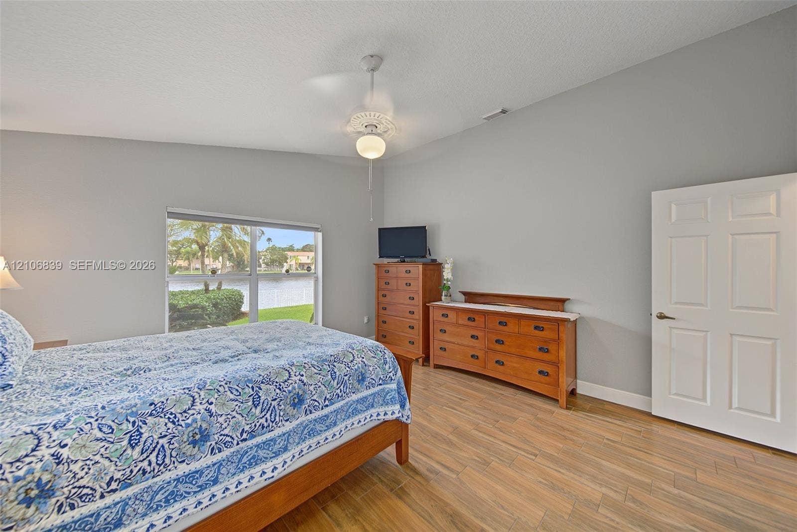 12683 NW 11th Place, Sunrise, FL 33323 Room featuring vaulted ceilings, wood-finish flooring, a central ceiling fan with integrated lighting, and a large window with exterior water surroundings