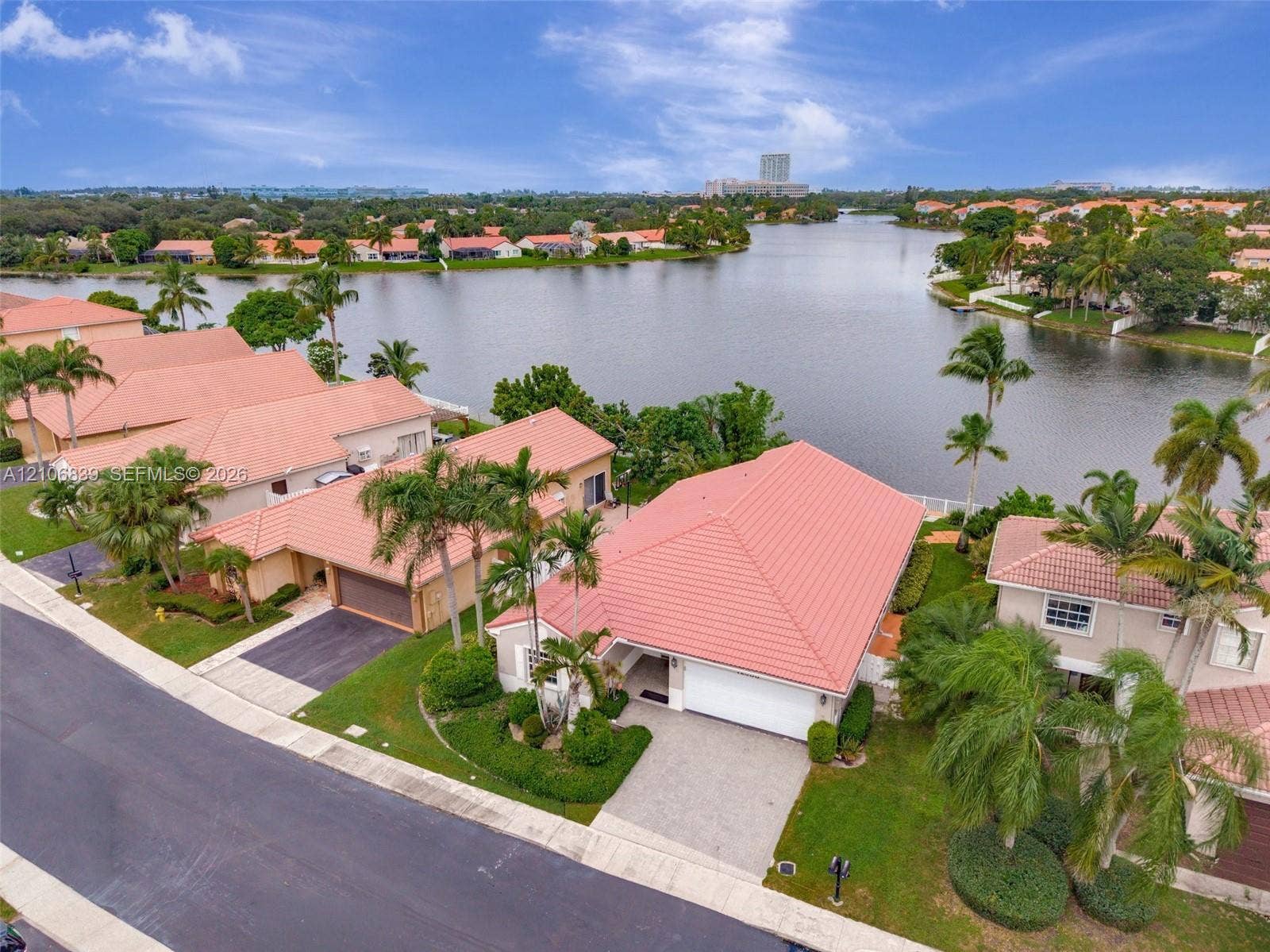 12683 NW 11th Place, Sunrise, FL 33323 Waterfront residential property featuring a tile roof, paved driveway, attached garage, and landscaped lawn with mature palms