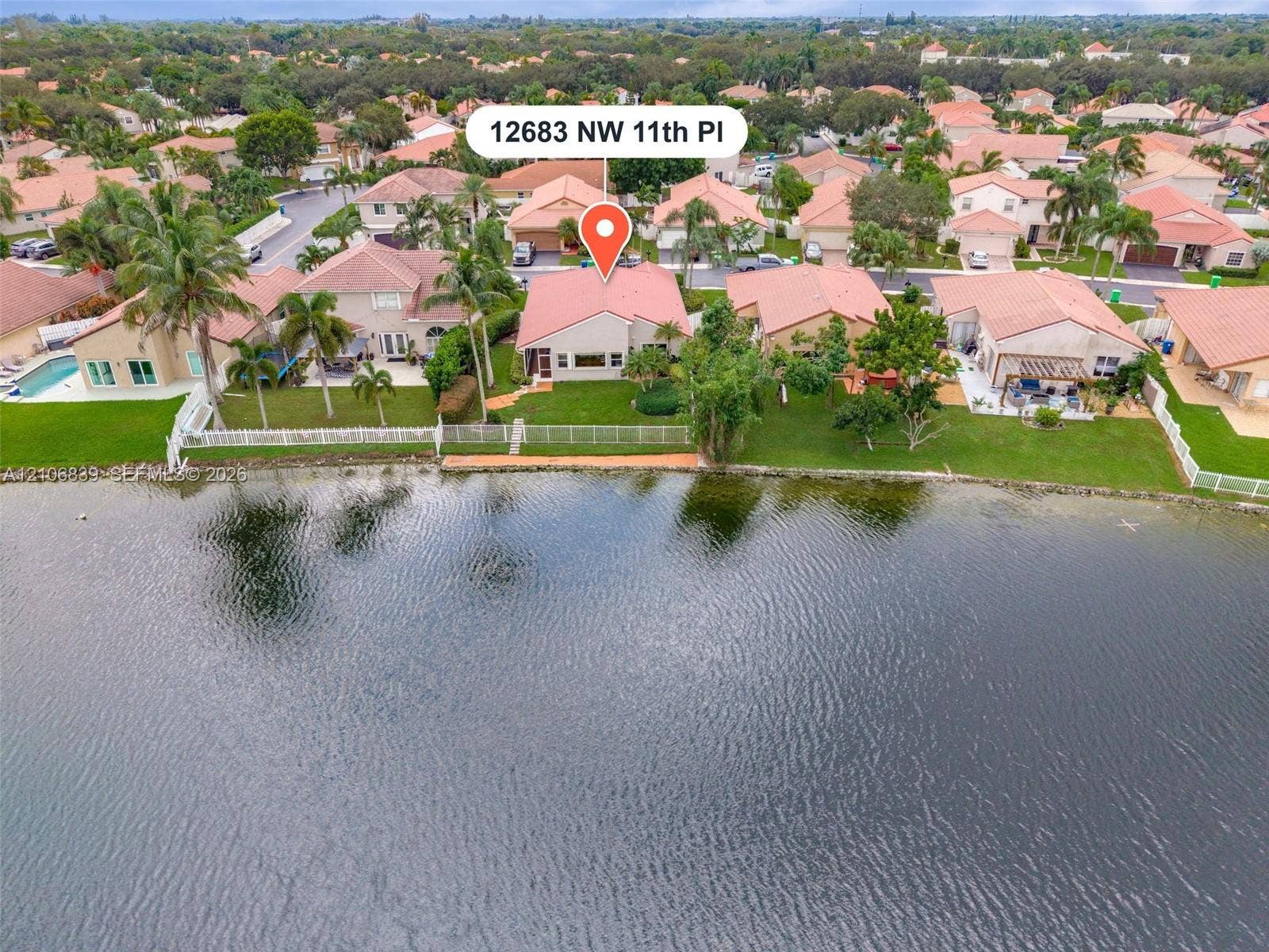 12683 NW 11th Place, Sunrise, FL 33323 Waterfront property featuring a tile roof, mature landscaping, and a fenced backyard