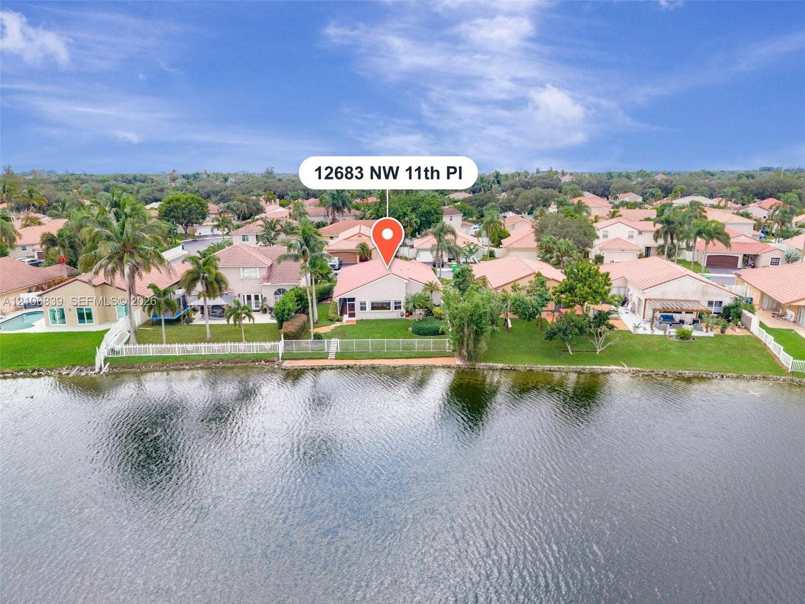 12683 NW 11th Place, Sunrise, FL 33323 Waterfront property featuring a grass lawn, mature trees, and perimeter fencing