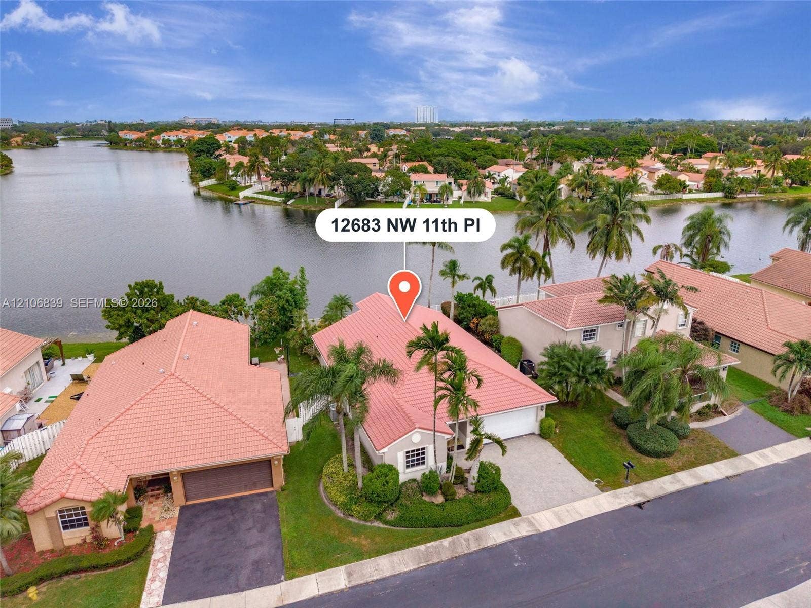 12683 NW 11th Place, Sunrise, FL 33323 Waterfront property featuring a tile roof, paved driveway, two-car garage, and established tropical landscaping