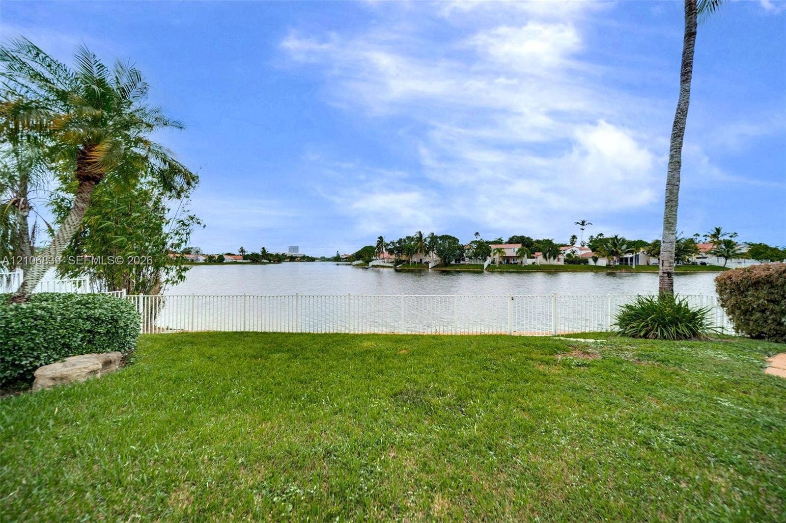 12683 NW 11th Place, Sunrise, FL 33323 Waterfront property featuring a manicured lawn, white metal perimeter fencing, mature palms, and expansive water frontage