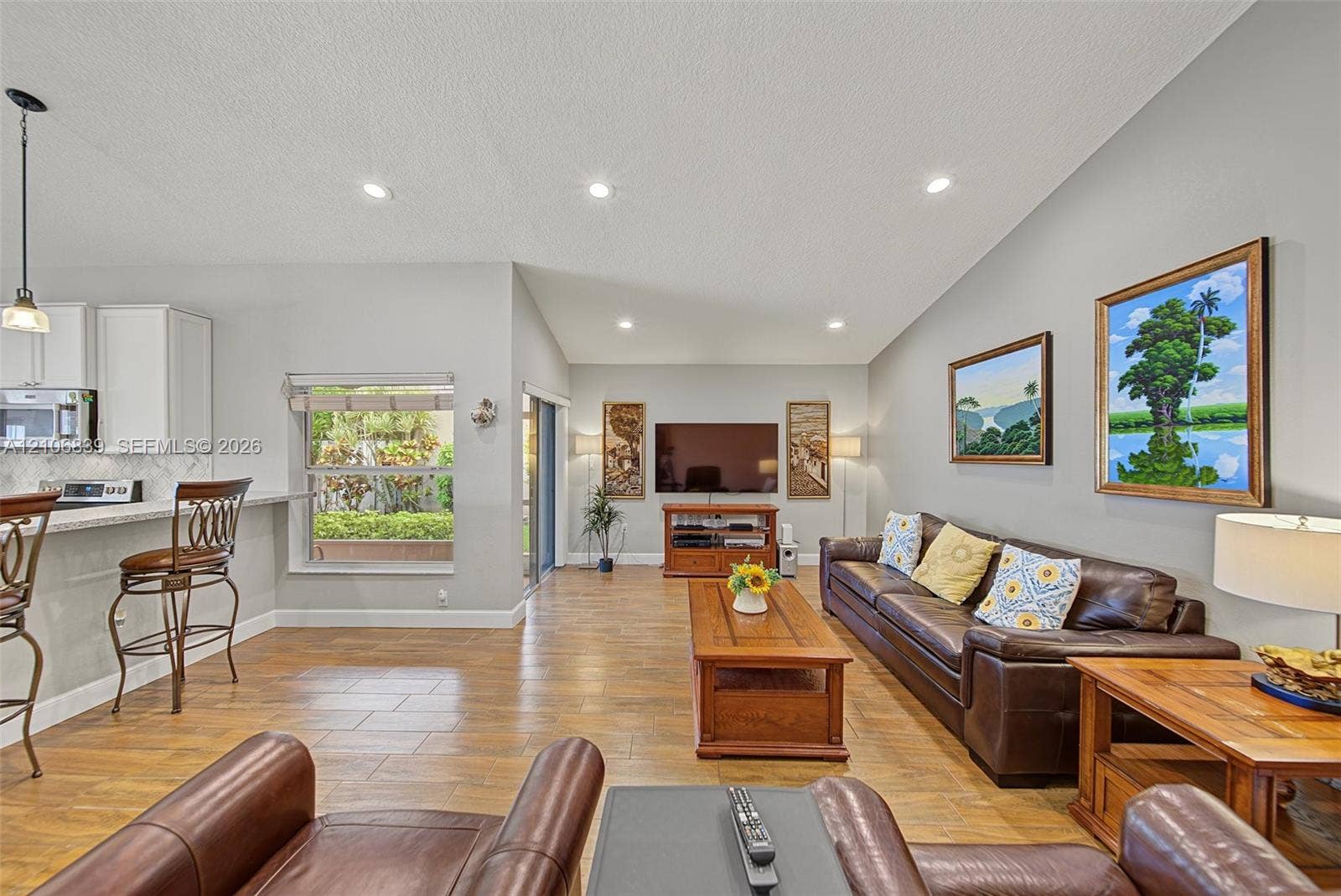 12683 NW 11th Place, Sunrise, FL 33323 Open-concept living space featuring vaulted ceilings, recessed lighting, wood-finish tile flooring, white cabinetry, and sliding glass doors