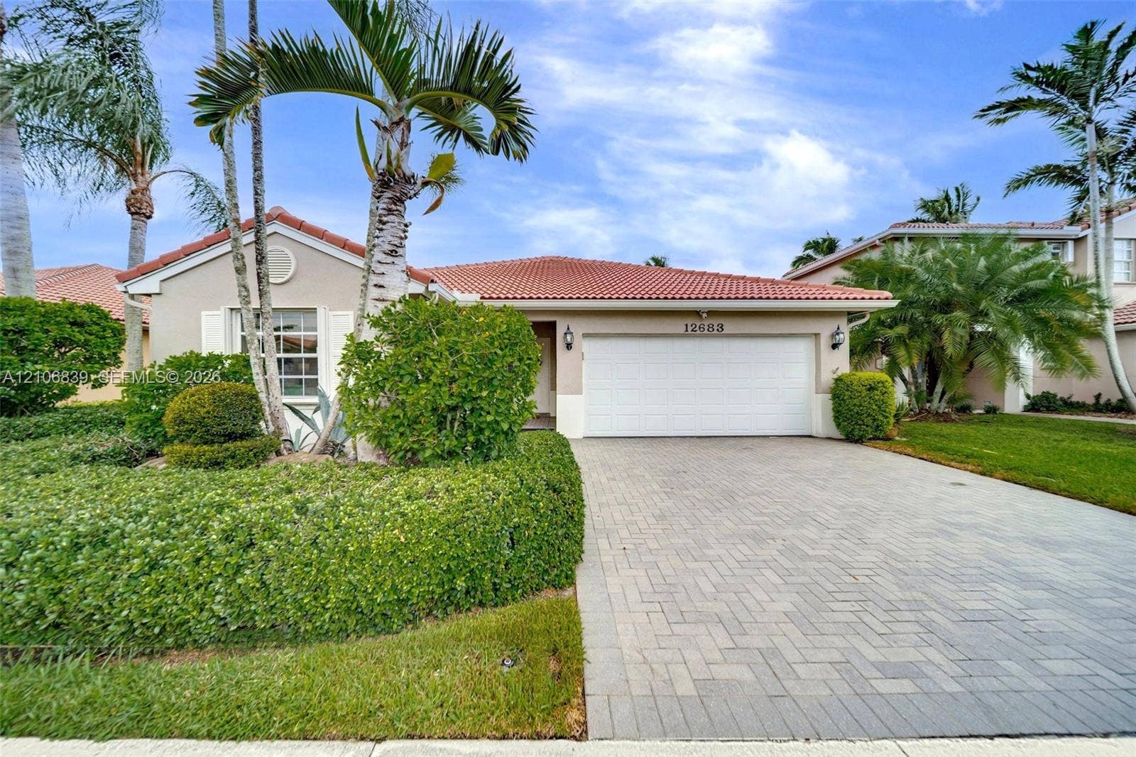 12683 NW 11th Place, Sunrise, FL 33323 Single-story residence featuring a terracotta-tiled roof, paver driveway, attached two-car garage, and manicured landscaping with mature palm trees