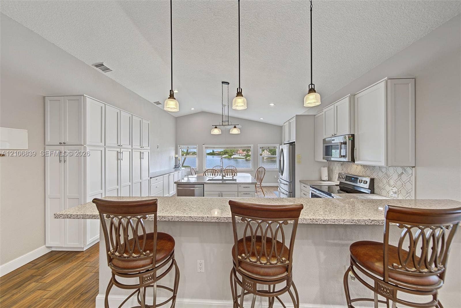 12683 NW 11th Place, Sunrise, FL 33323 Kitchen featuring a vaulted ceiling, quartz countertops, white cabinetry, three pendant lights, and wood-finish flooring