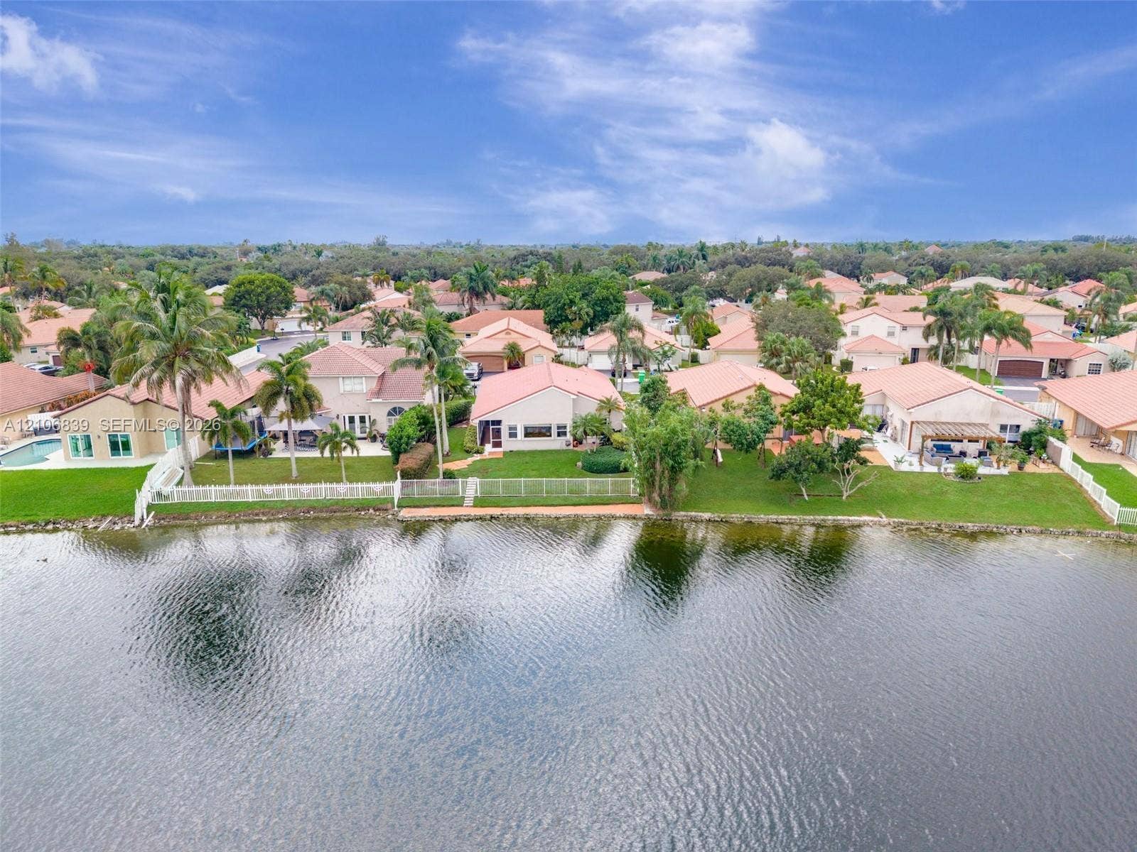 12683 NW 11th Place, Sunrise, FL 33323 Waterfront property featuring a manicured lawn, white perimeter fencing, and mature palm trees