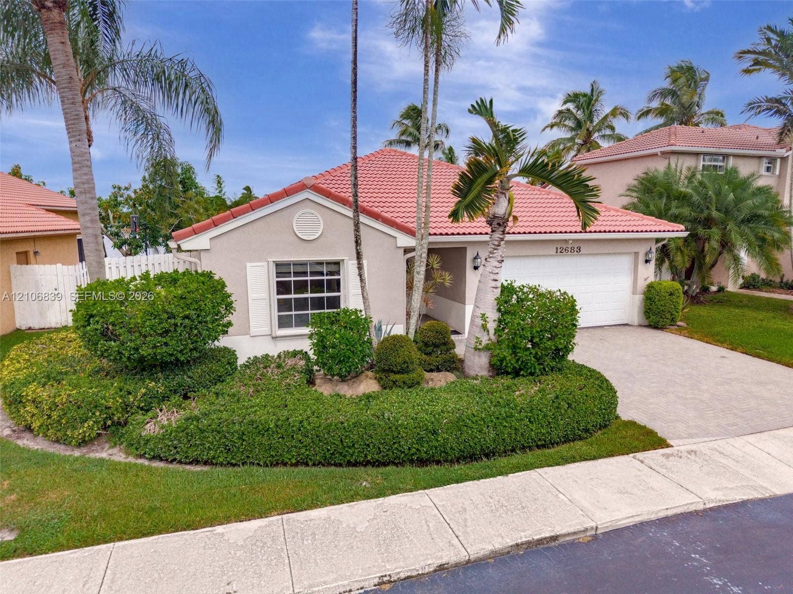 12683 NW 11th Place, Sunrise, FL 33323 Stucco exterior featuring a terracotta-tile roof, paved driveway, window shutters, and established tropical landscaping