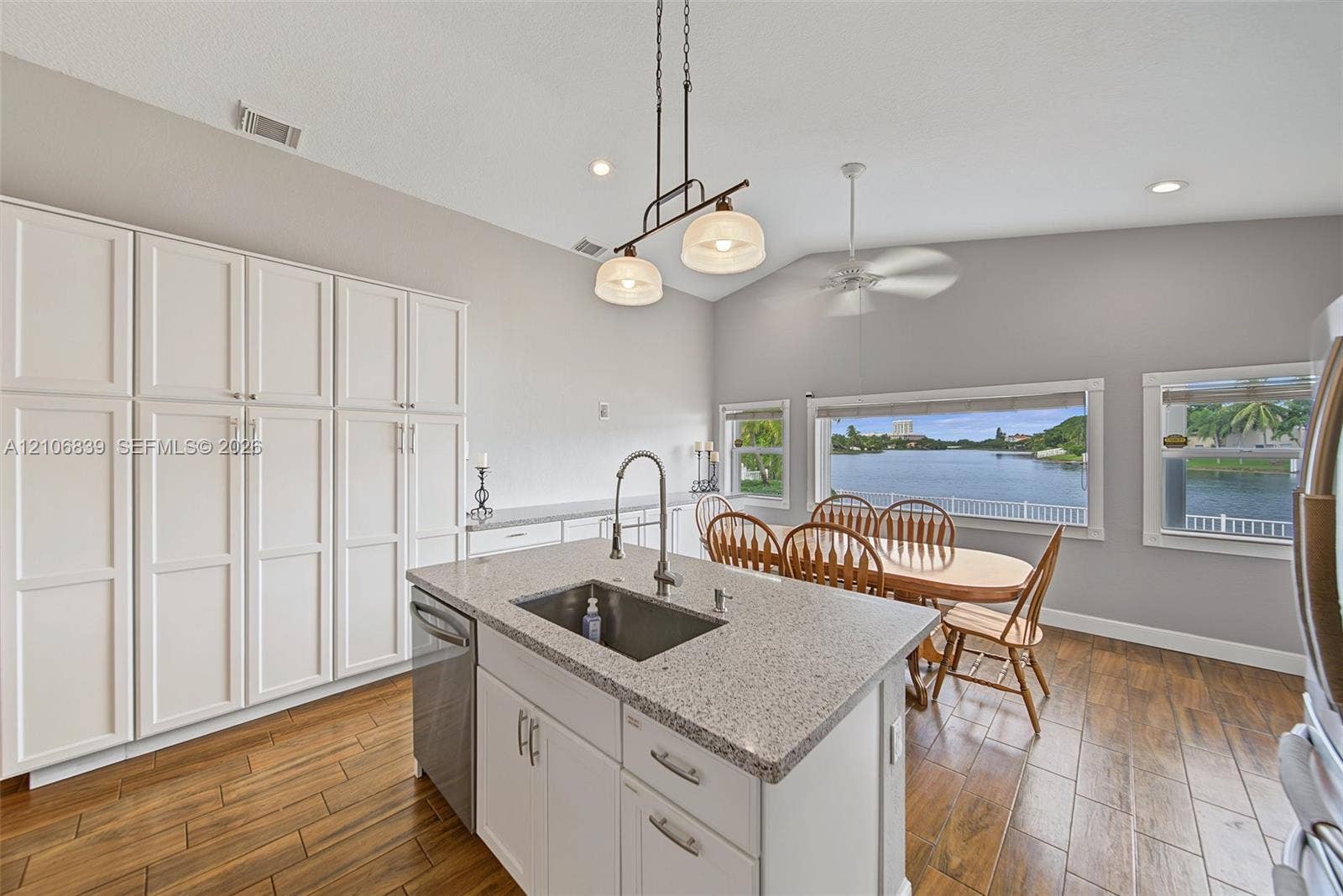 12683 NW 11th Place, Sunrise, FL 33323 Kitchen featuring white floor-to-ceiling cabinetry, a center island with a stone countertop and integrated sink, wood-finish flooring, vaulted ceilings, and large windows with water scenery