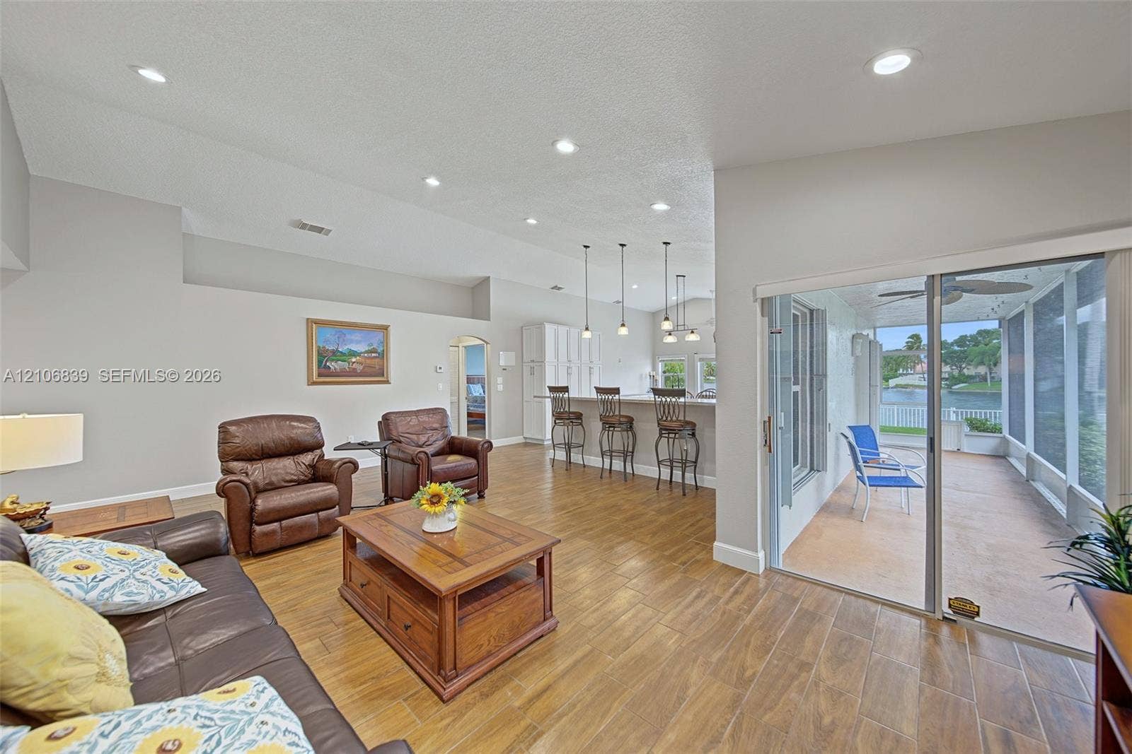12683 NW 11th Place, Sunrise, FL 33323 Open-concept interior featuring wood-finish tile flooring, recessed lighting, breakfast bar with pendant lighting, and sliding glass doors leading to a screened-in patio