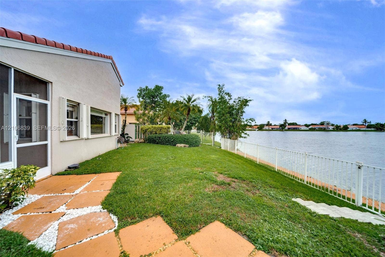 12683 NW 11th Place, Sunrise, FL 33323 Waterfront exterior featuring a manicured lawn, stone paver pathway, and perimeter metal fencing