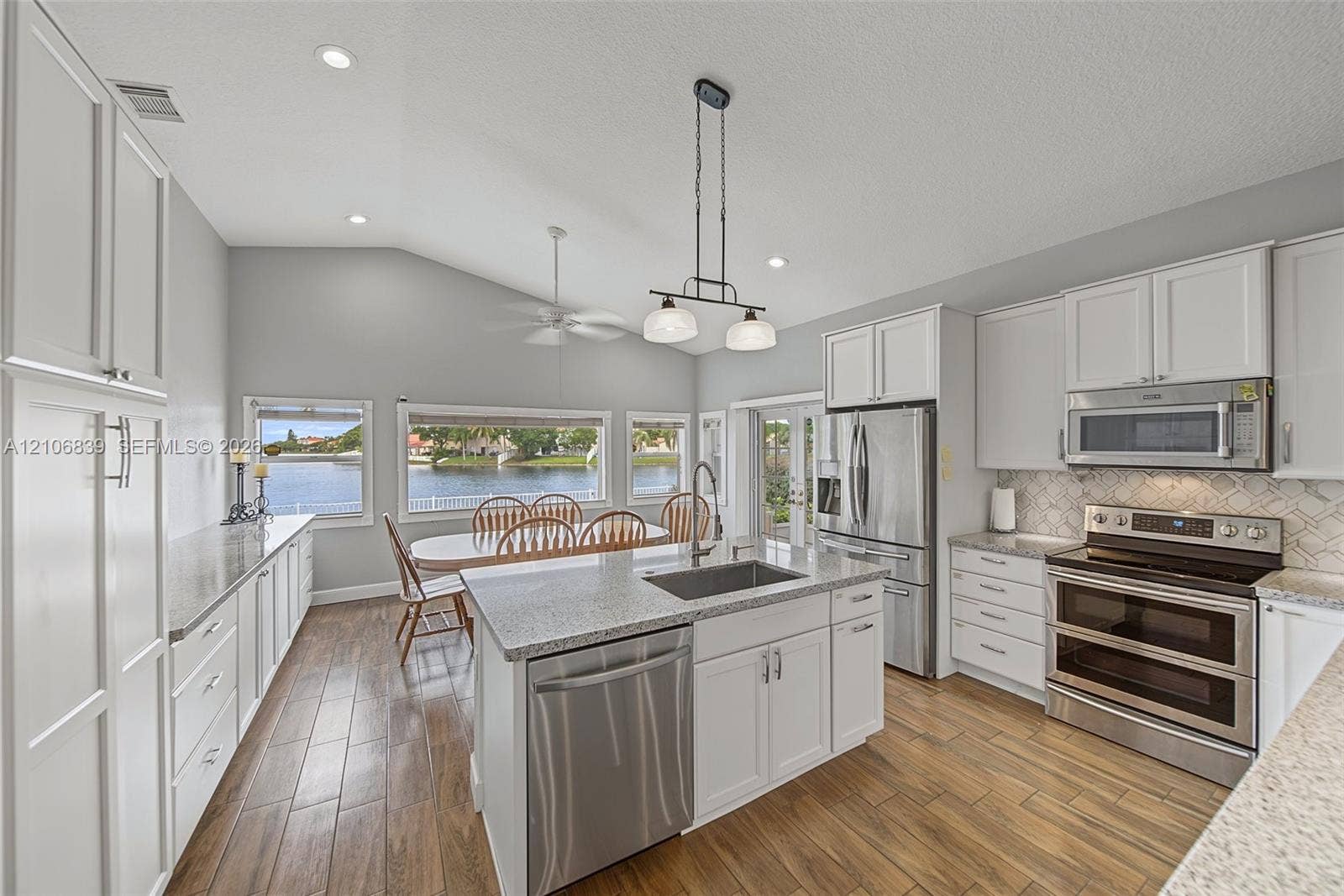 12683 NW 11th Place, Sunrise, FL 33323 Kitchen featuring vaulted ceilings, wood-finish flooring, a central island with a stainless steel undermount sink, quartz countertops, and stainless steel appliances