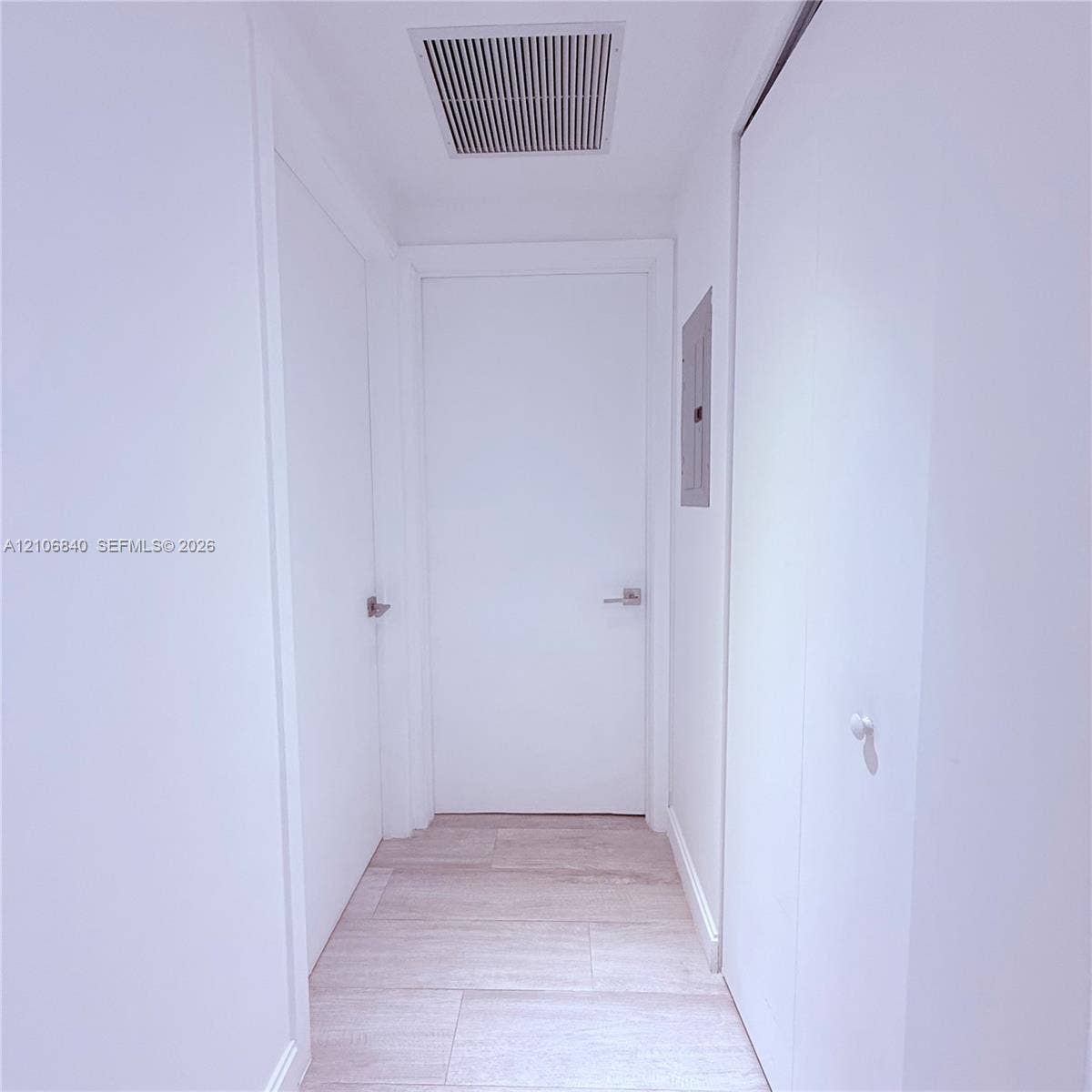 Hallway featuring light-toned wood-finish flooring, solid-core doors with brushed metal lever handles, and neutral wall finishes