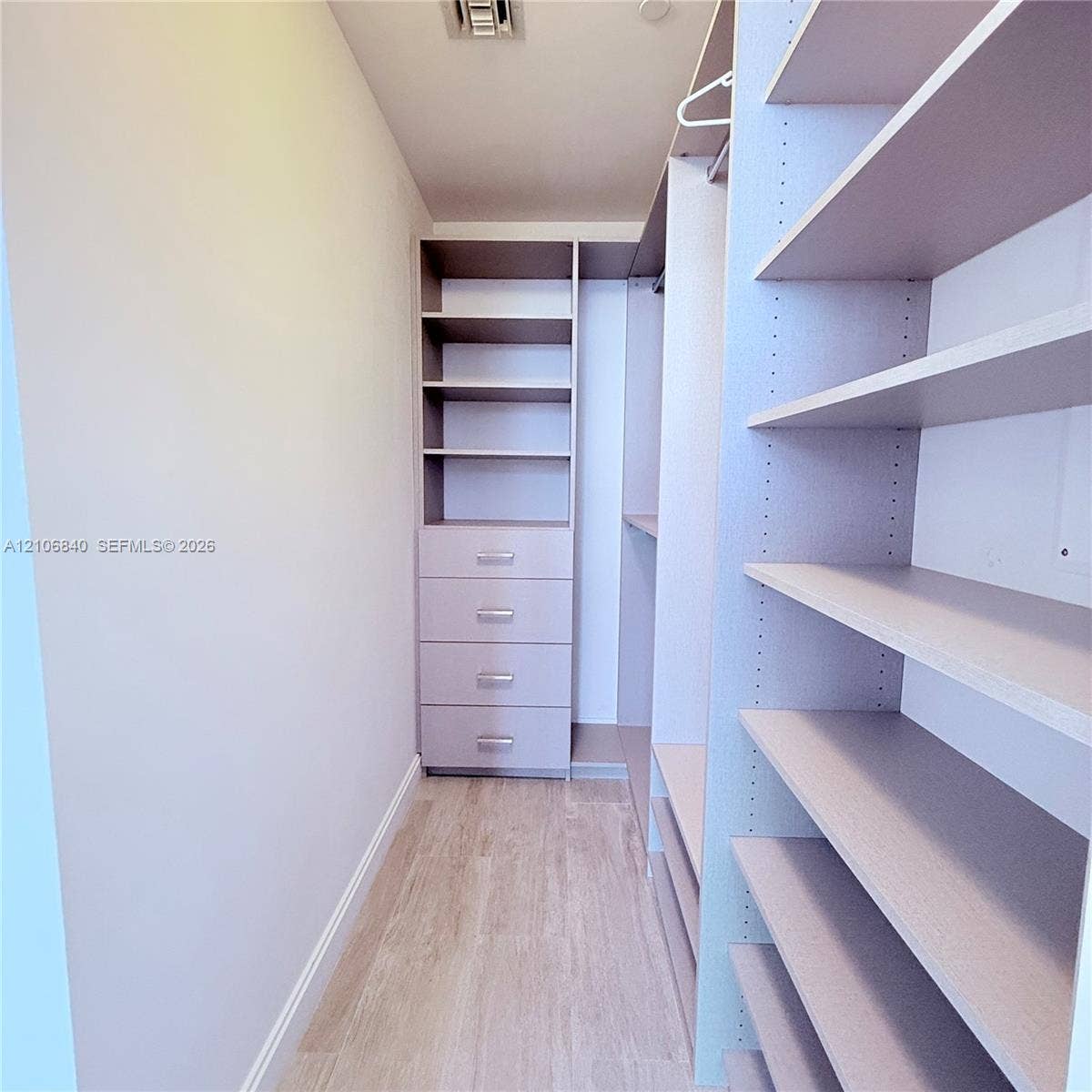 Walk-in closet featuring built-in shelving, four pull-out drawers with metallic hardware, integrated hanging rods, and wood-finish flooring