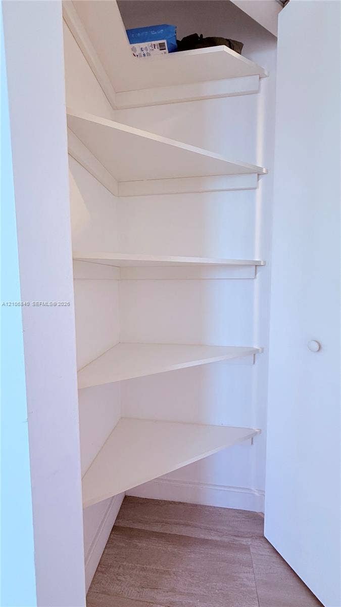 Built-in storage closet featuring tiered corner shelving and wood-finish flooring