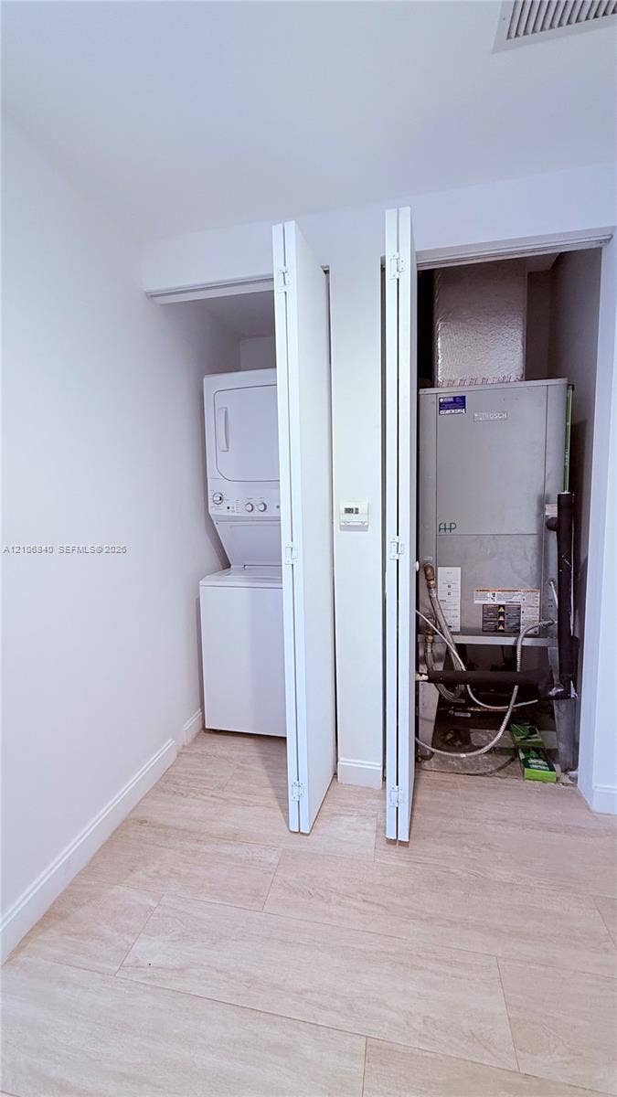 Utility closet featuring a stacked washer and dryer unit, HVAC equipment, and light-toned wood-finish flooring