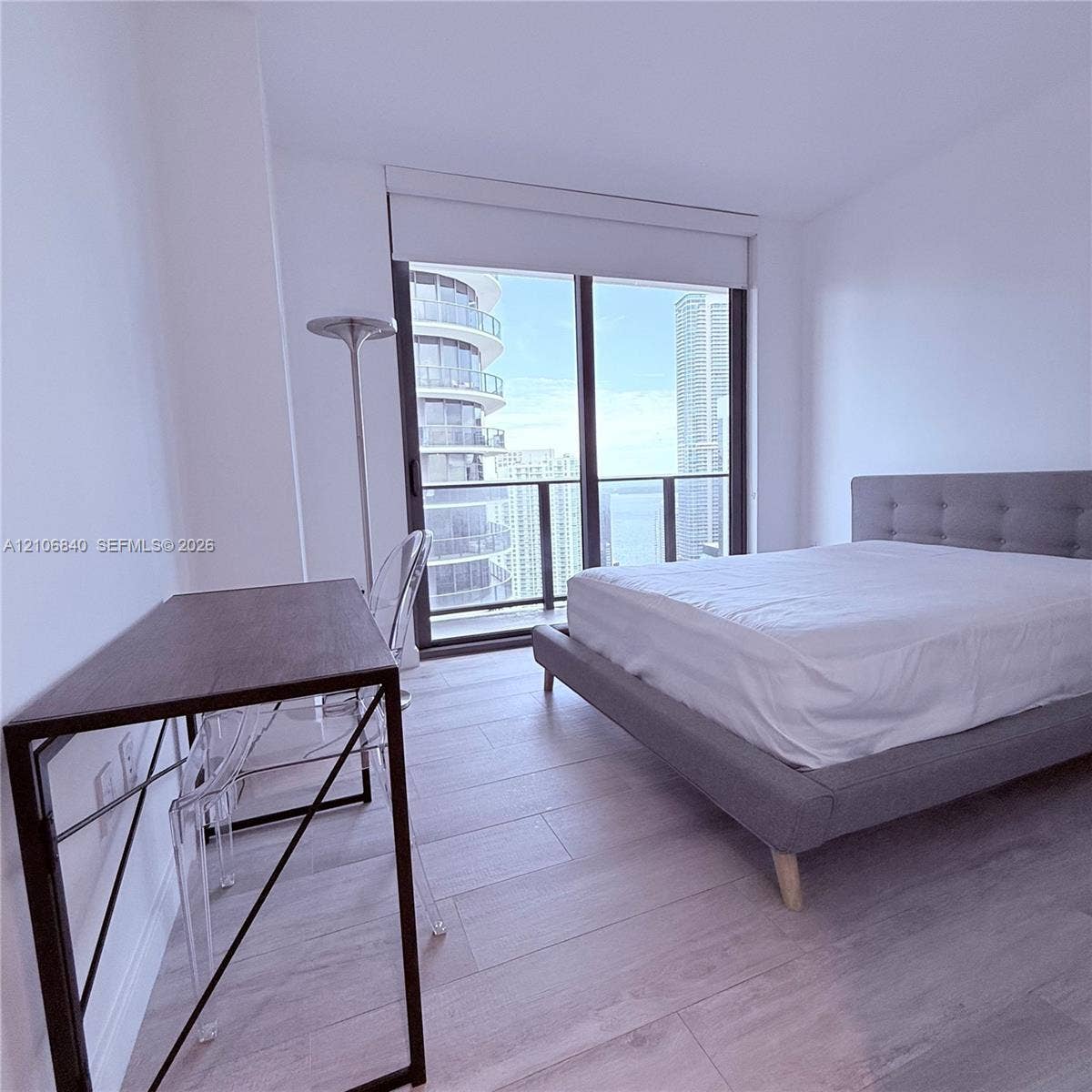 Floor-to-ceiling windows with roller shades, wood-finish flooring, and a private balcony featuring a glass-panel railing