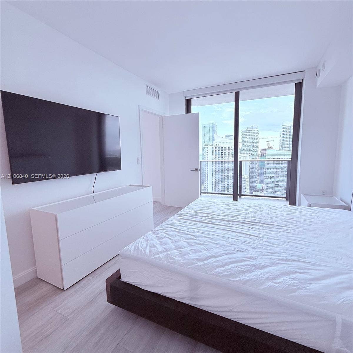 Floor-to-ceiling glass sliding doors, private balcony, wood-finish flooring, and neutral wall palette