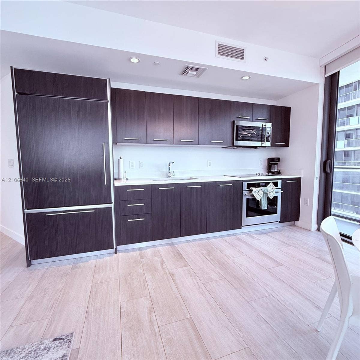 Kitchen featuring dark-finish cabinetry, light-toned stone-surface countertops, wood-finish flooring, and integrated stainless-steel appliances