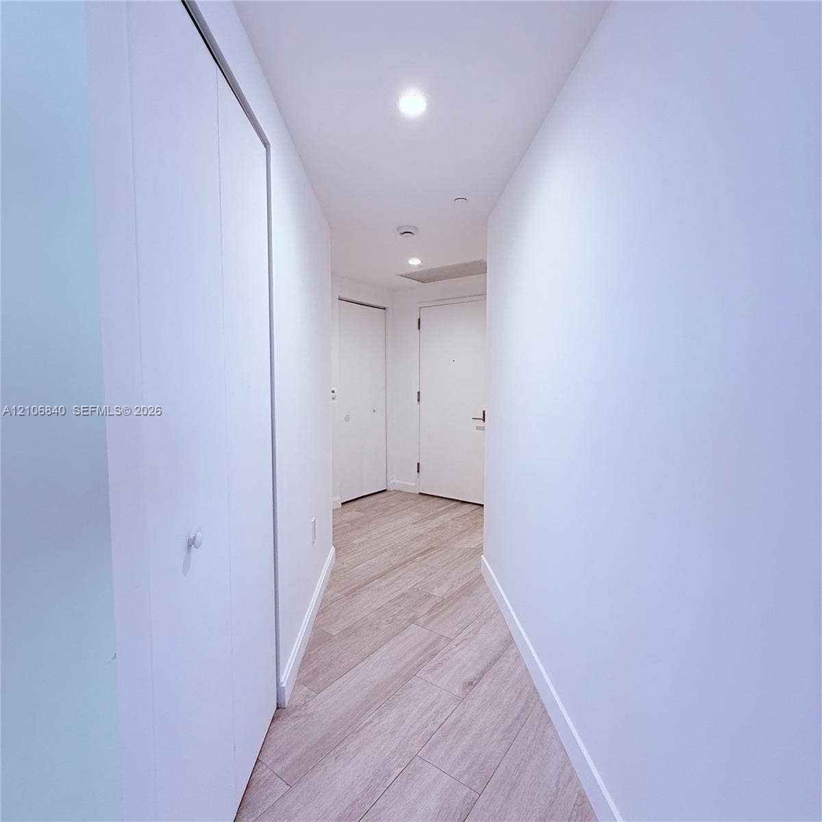Hallway featuring wood-finish flooring, recessed lighting, and multiple interior closet doors with white hardware