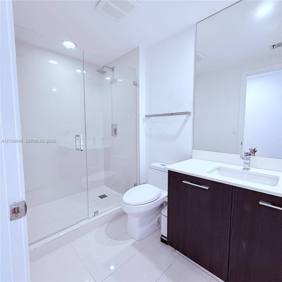 Bathroom featuring a glass-enclosed walk-in shower, dark-toned vanity with a light-colored countertop, integrated rectangular sink, and floor-to-ceiling mirror