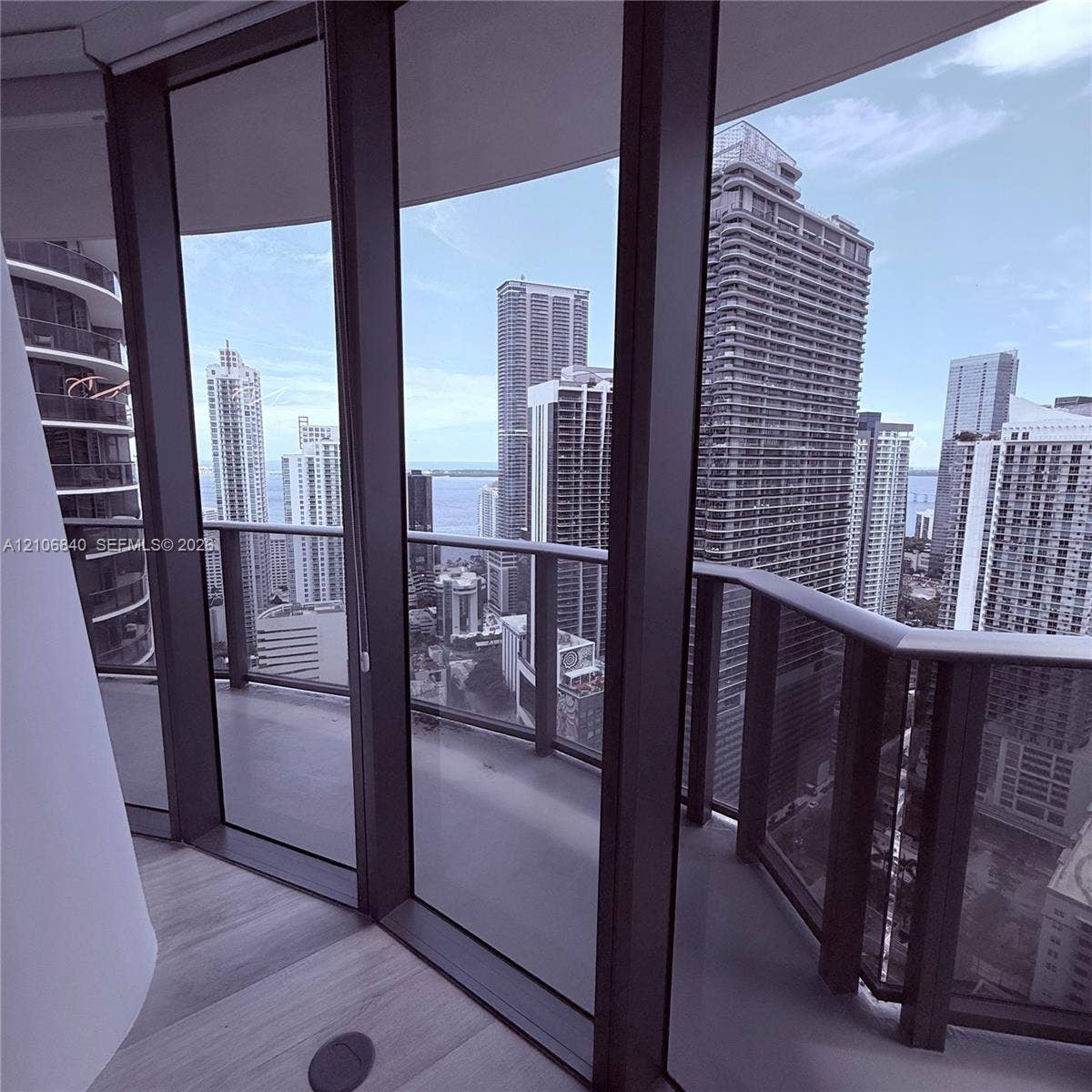 Floor-to-ceiling glass paneling, wraparound balcony with metal railings, and wood-finish flooring