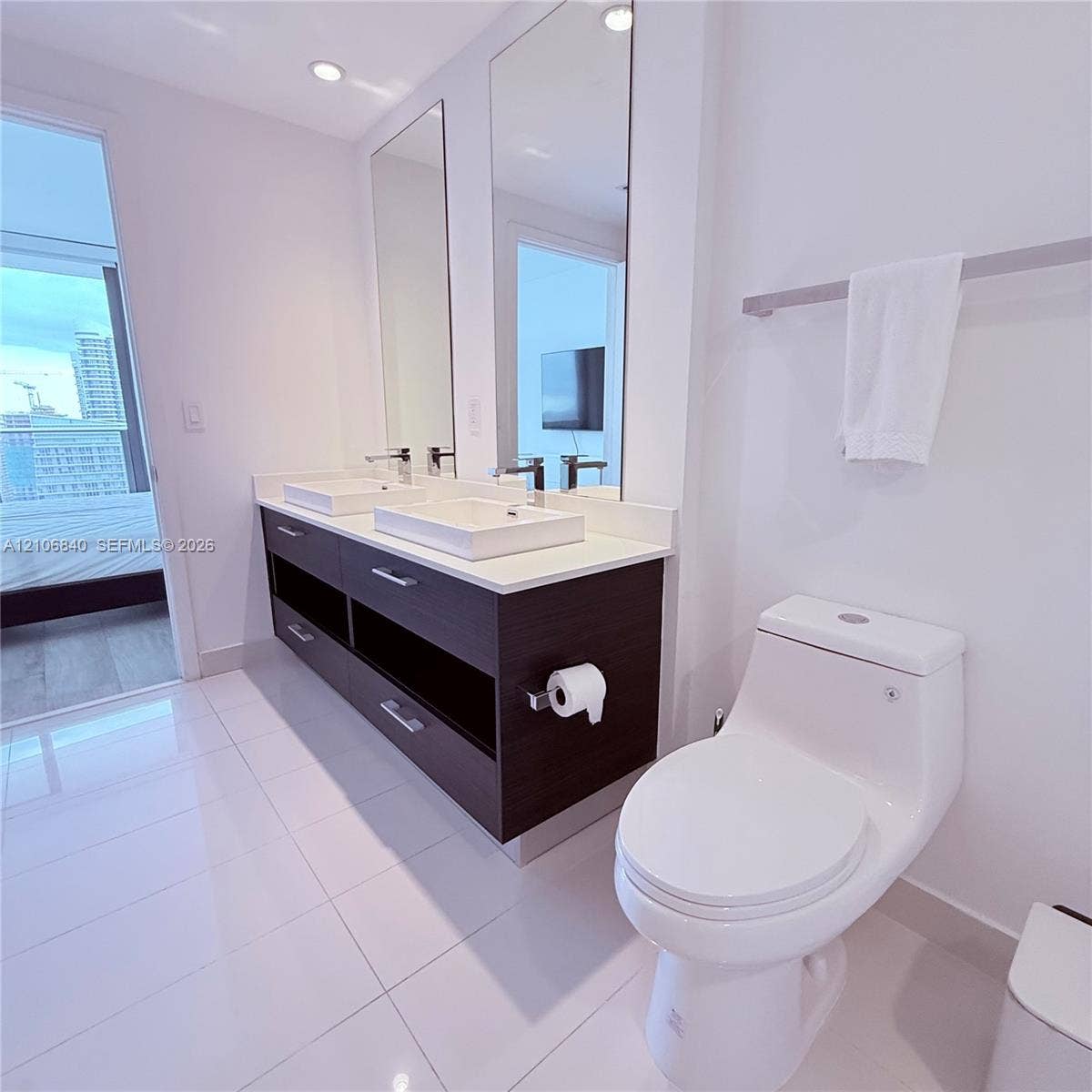 Dual-vanity cabinet featuring a dark wood-finish, stone-surfaced countertop, square vessel sinks, polished chrome fixtures, and full-length vertical mirrors, complemented by white tile flooring