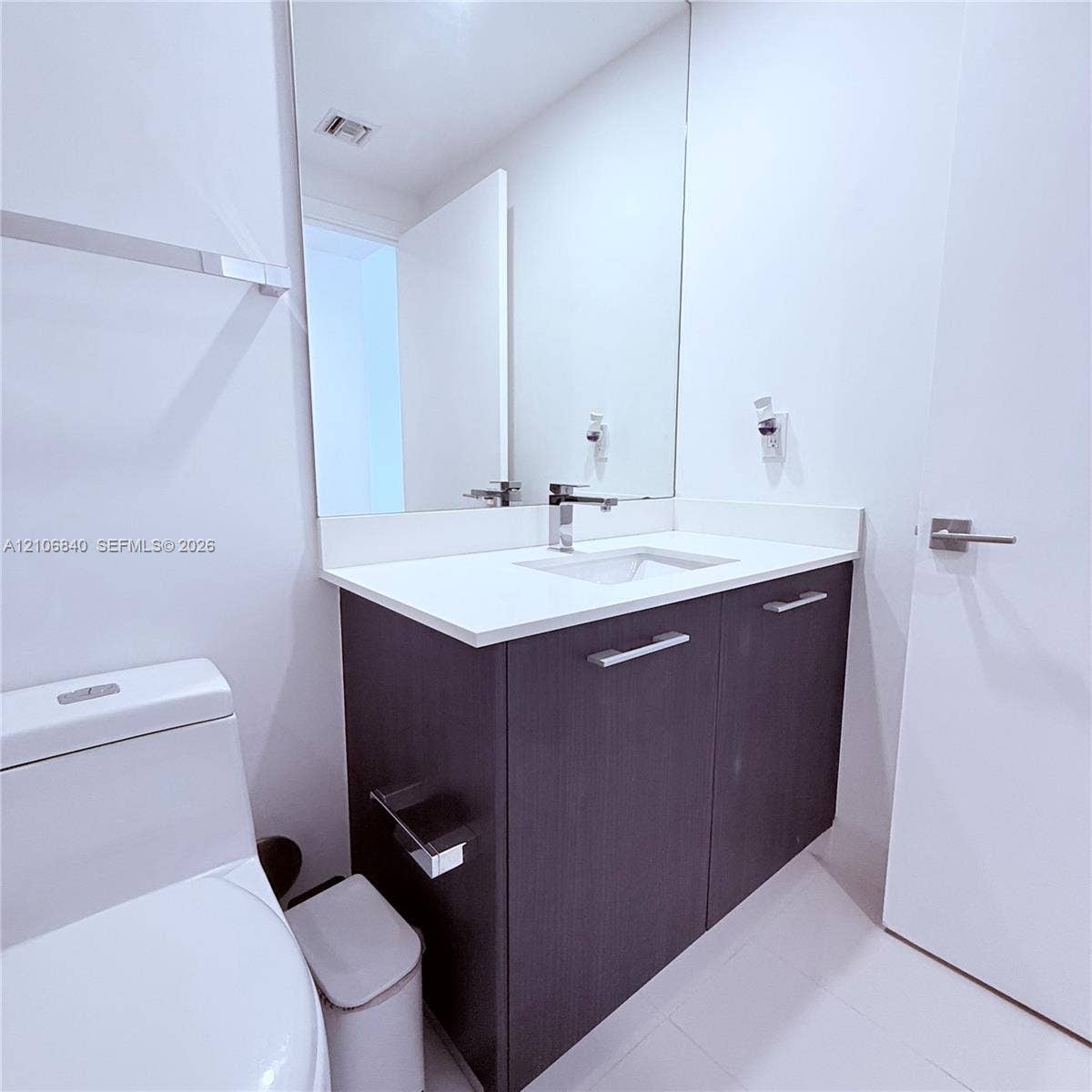 Bathroom featuring a dark wood-finish vanity, solid white countertop with an integrated basin, chrome-finish faucet, and full-height wall mirror