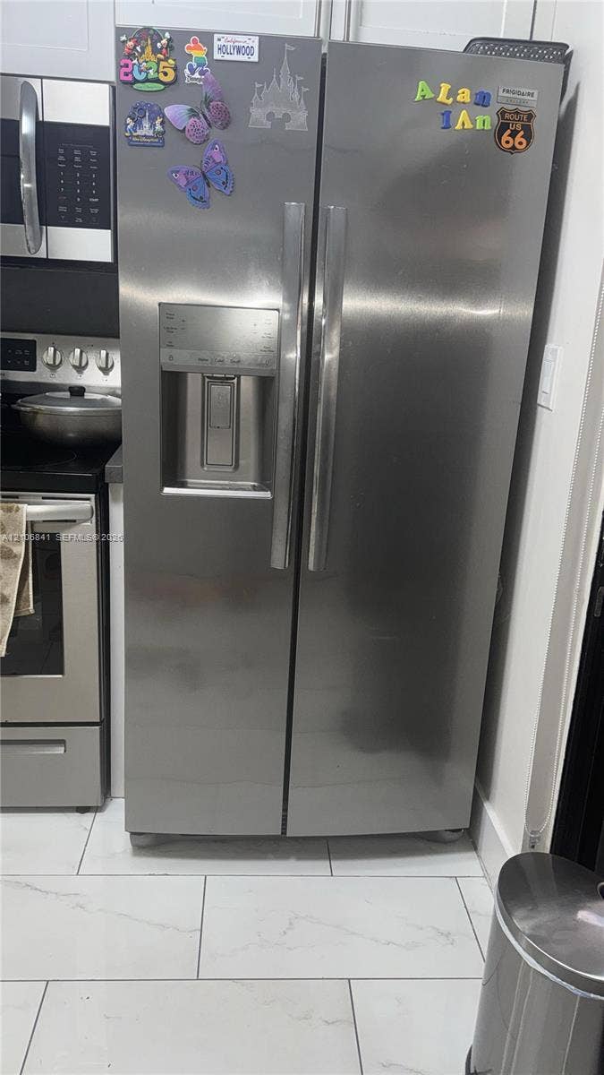 Stainless steel side-by-side refrigerator with external ice and water dispenser, paired with matching stainless steel range and over-the-range microwave, complemented by large-format tile flooring